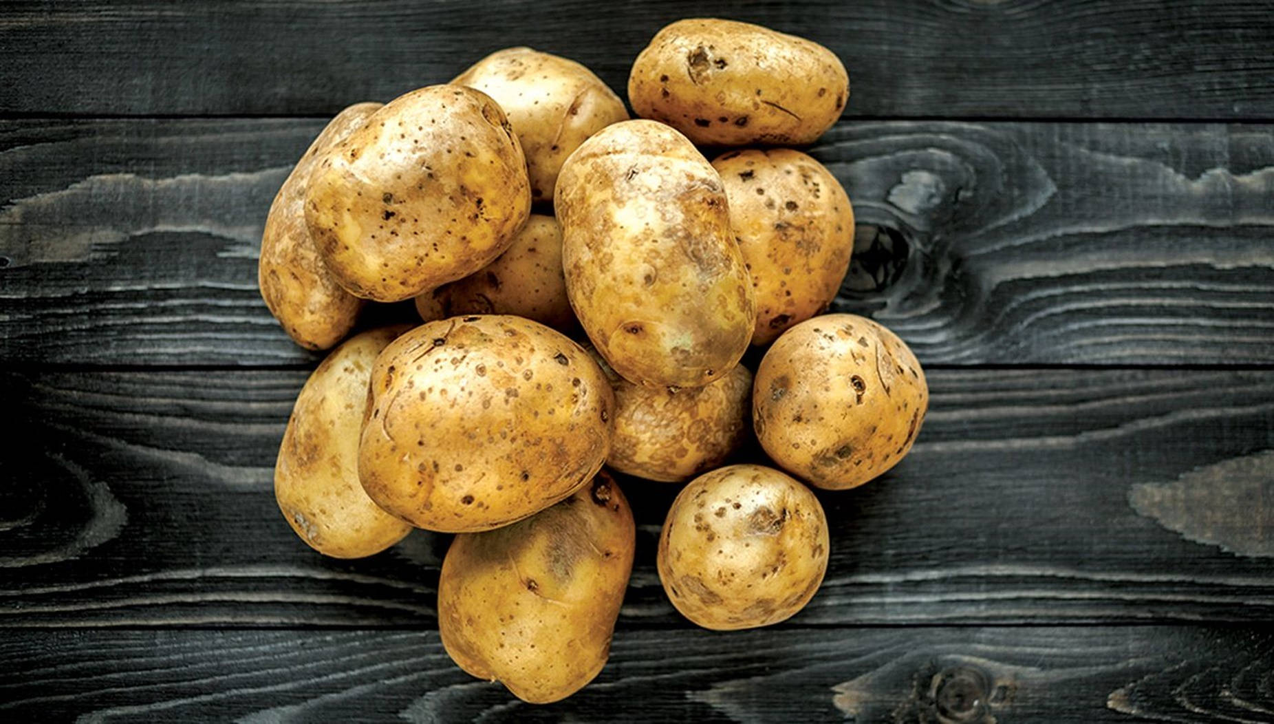 Potato 桌布 壁紙 — 一堆樸實的棕色馬鈴薯放在深色、風化的木質表面上，木紋清晰可見。