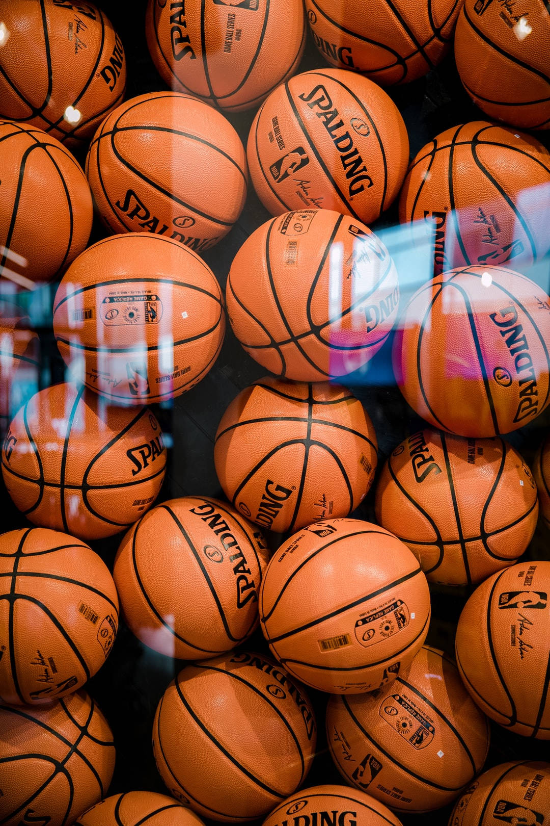 高清籃球 桌布 壁紙 — 一堆橙色 Spalding 籃球填滿畫面，其光滑表面反射出彩色燈光。