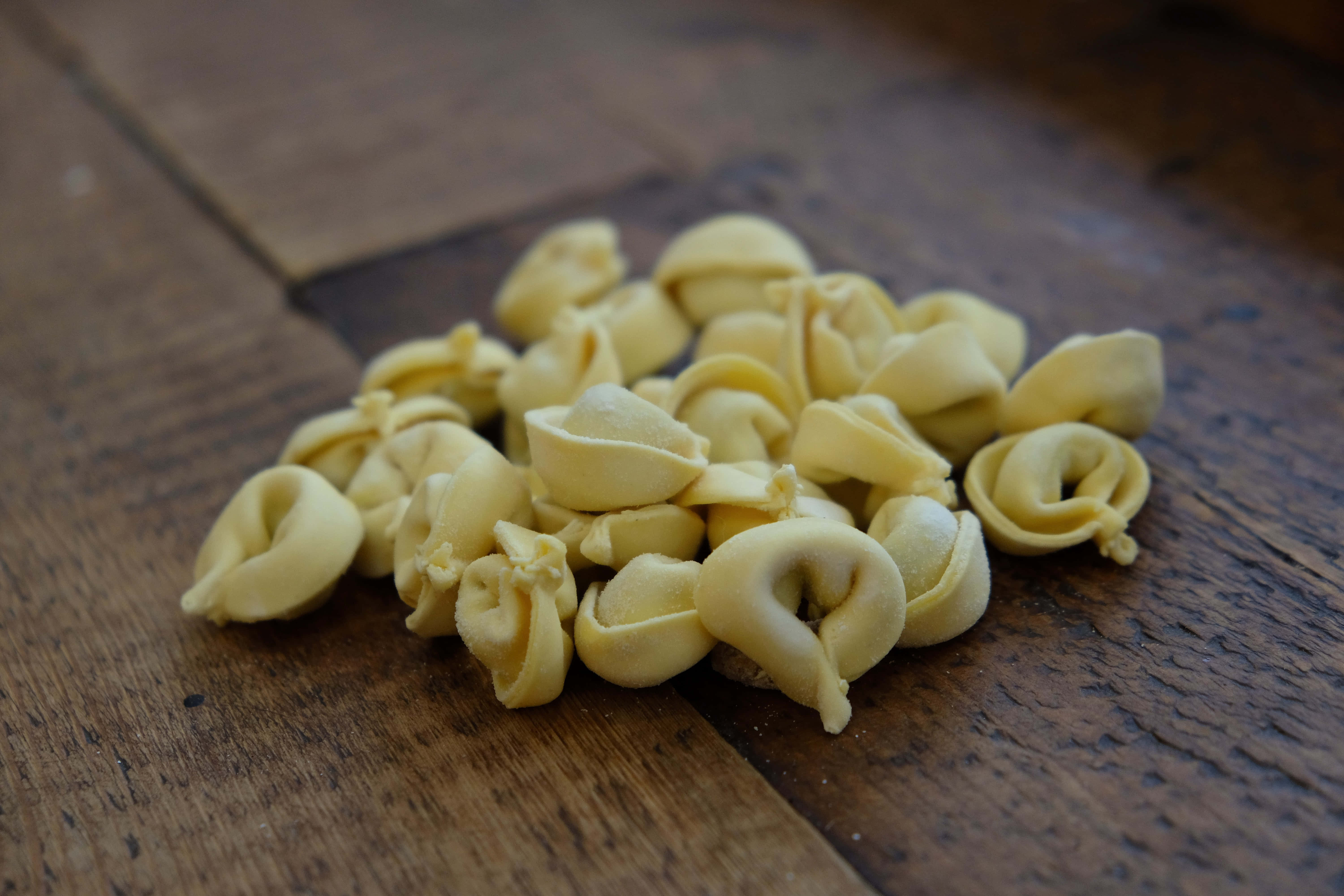 Pasta 桌布 壁紙 — 一堆淡黃色義大利餃子放在質樸的木質表面上，伴隨著溫暖的自然光線。
