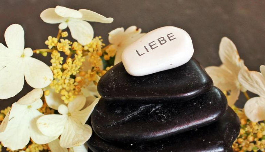 Meditation 桌布 壁紙 — 一堆深色拋光石頭，頂部有一塊刻有'LIEBE'的白色石頭，周圍環繞著白色和黃色的繡球花。
