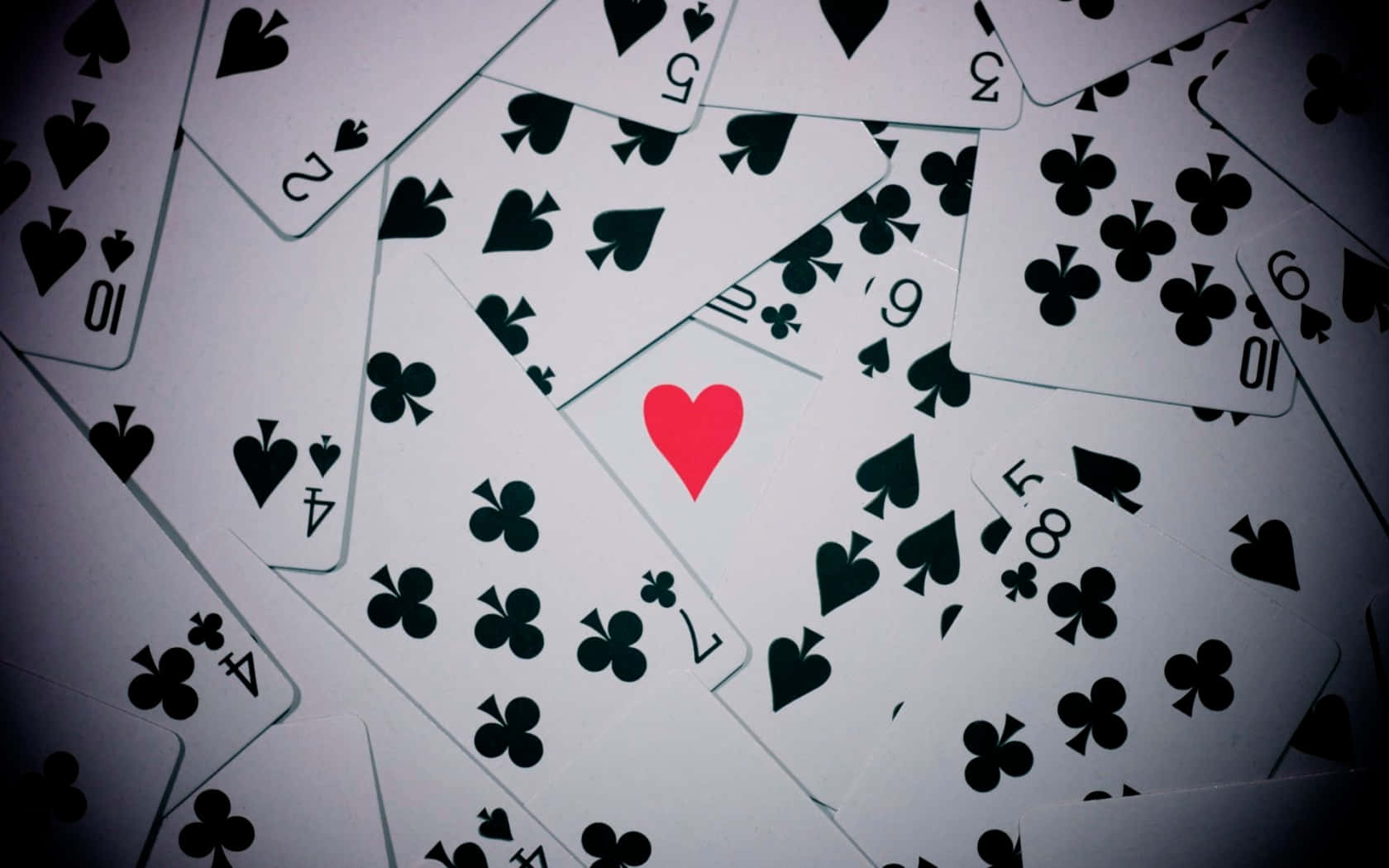 Playing Cards 桌布 壁紙 — 一堆混亂的撲克牌，其中一張紅心牌在黑色花色中脫穎而出。