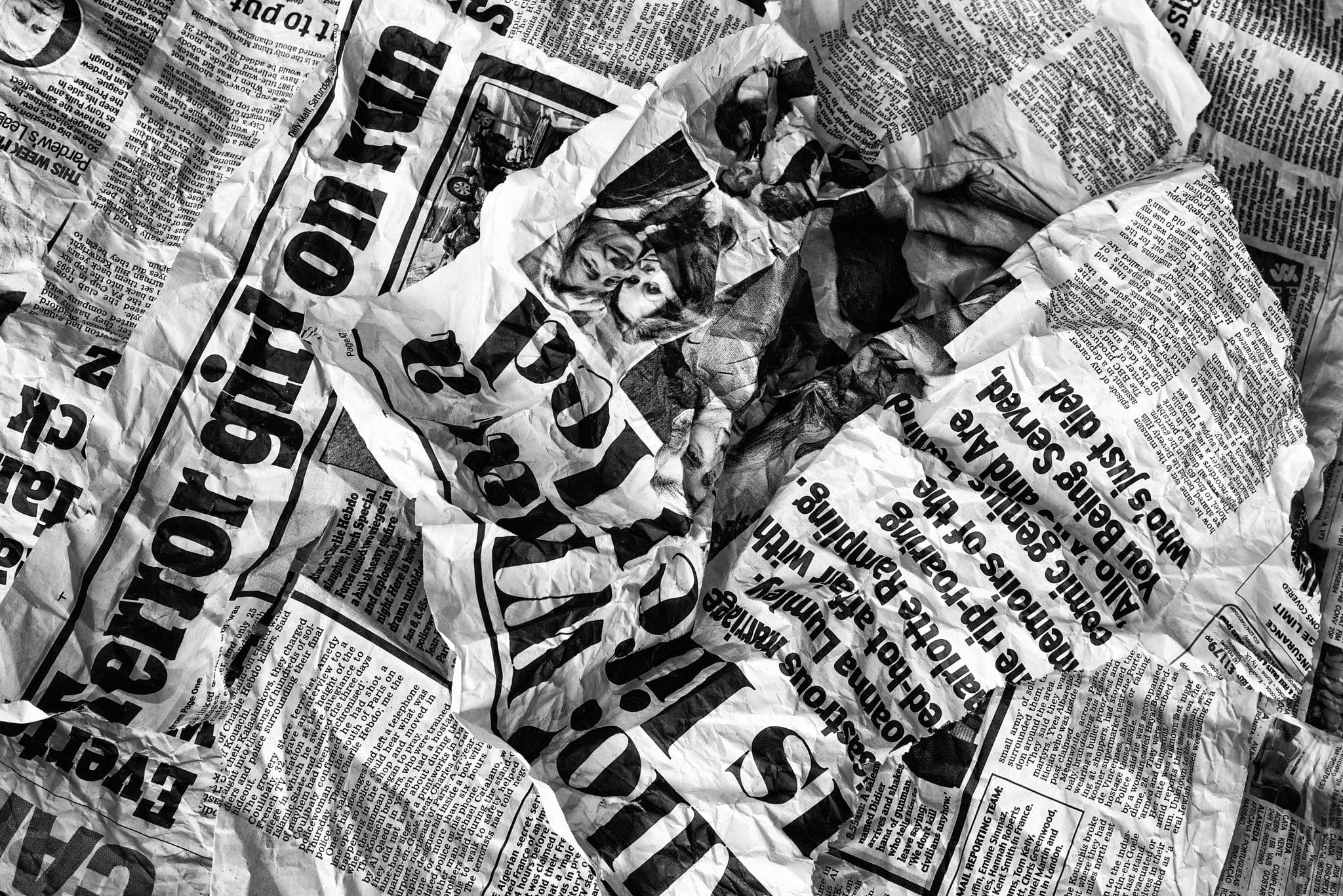 Newspaper 桌布 壁紙 — 一堆混亂的皺巴巴黑白報紙，帶有粗體標題和褪色照片，營造出粗糙的紋理表面。