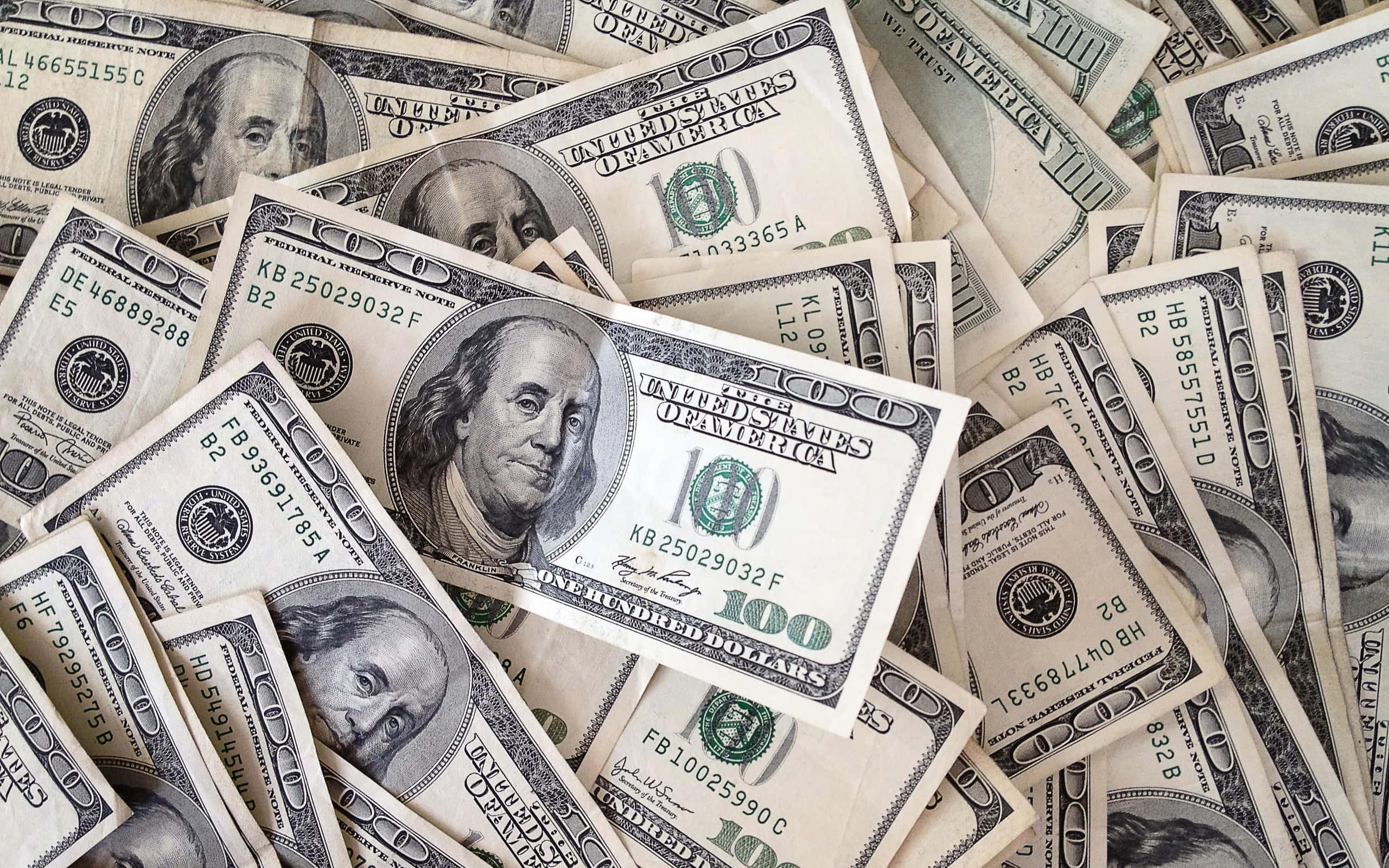 金錢 桌布 壁紙 — 一堆混亂的美國一百美元鈔票散亂地堆放，多張鈔票上可見班傑明·富蘭克林的肖像。