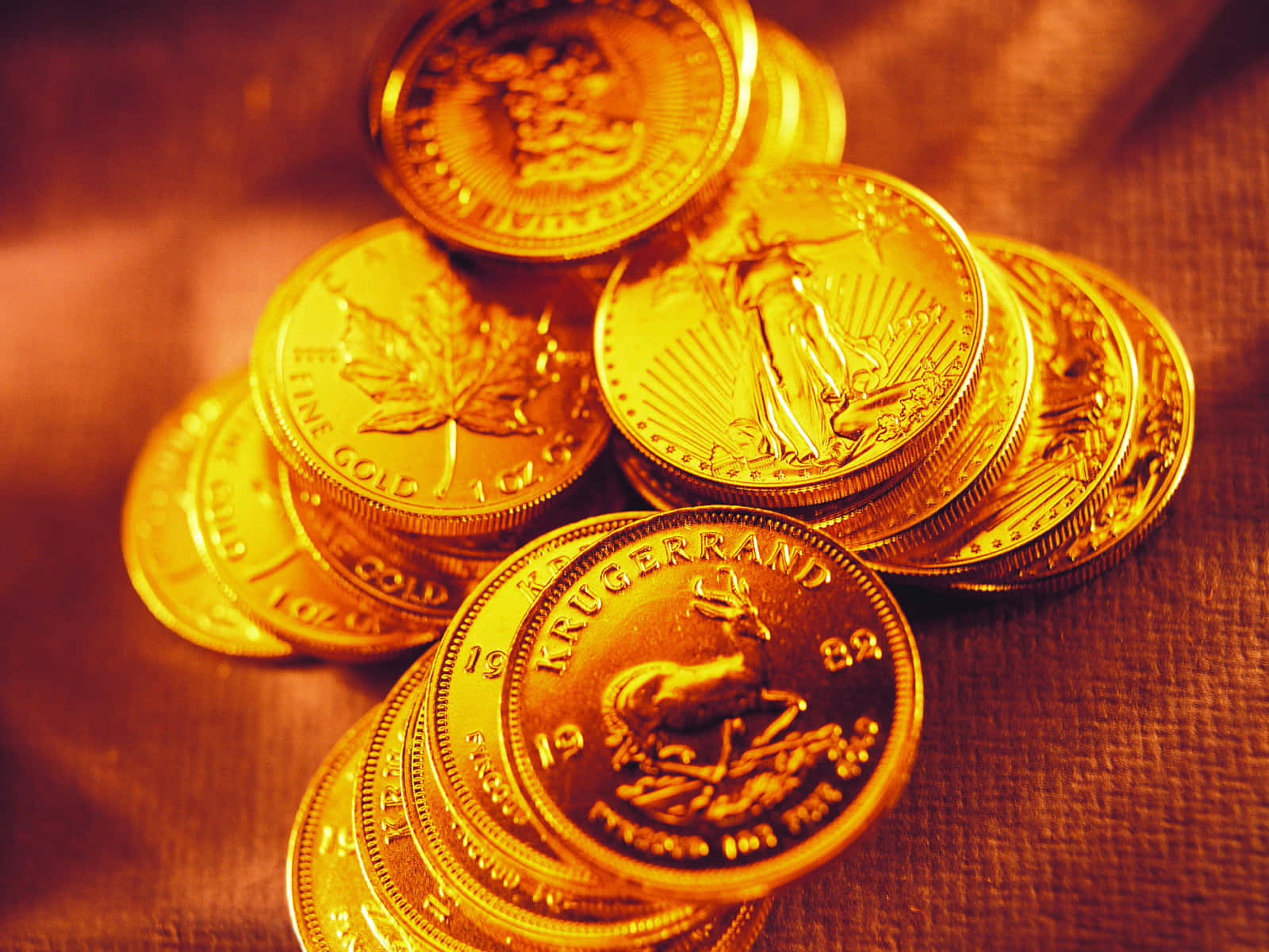 金色動態 桌布 壁紙 — 一堆溫暖發光的金幣Krugerrand放在有紋理的布料表面上。