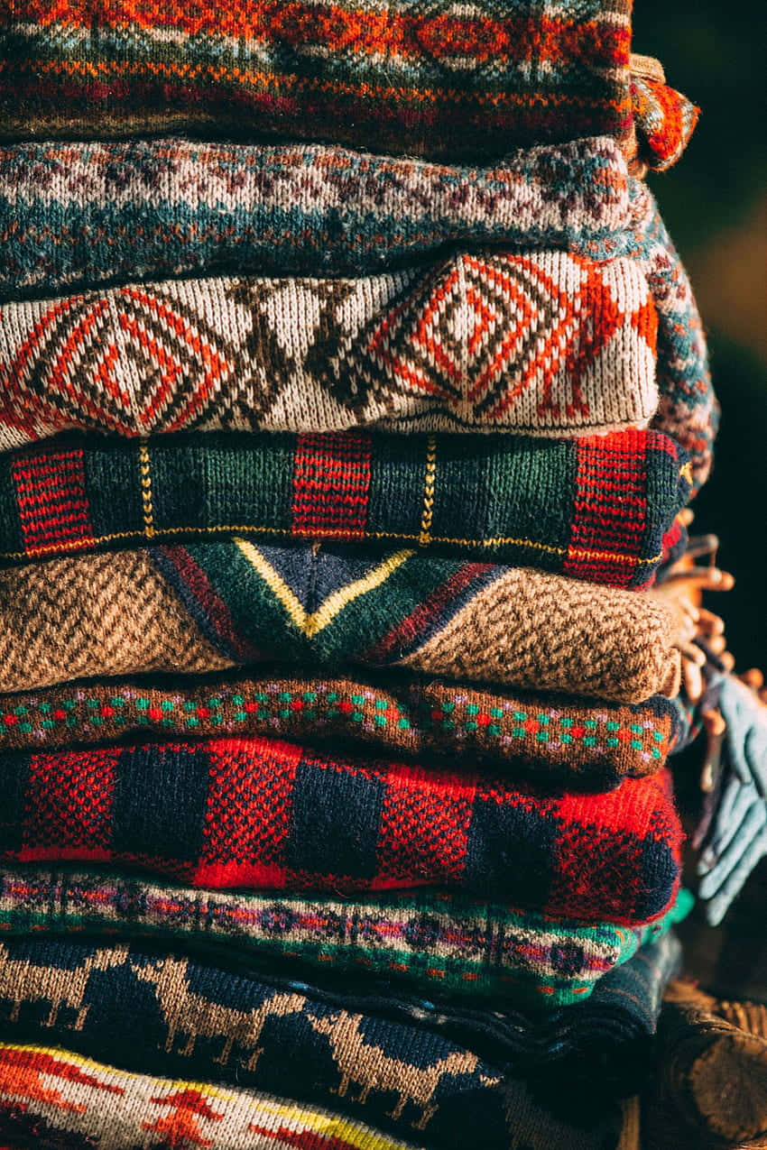clothing 桌布 壁紙 — 一堆溫暖的複雜圖案針織毛衣，呈現豐富的紅色、棕色和綠色色調，在柔和的金色光芒下閃耀。