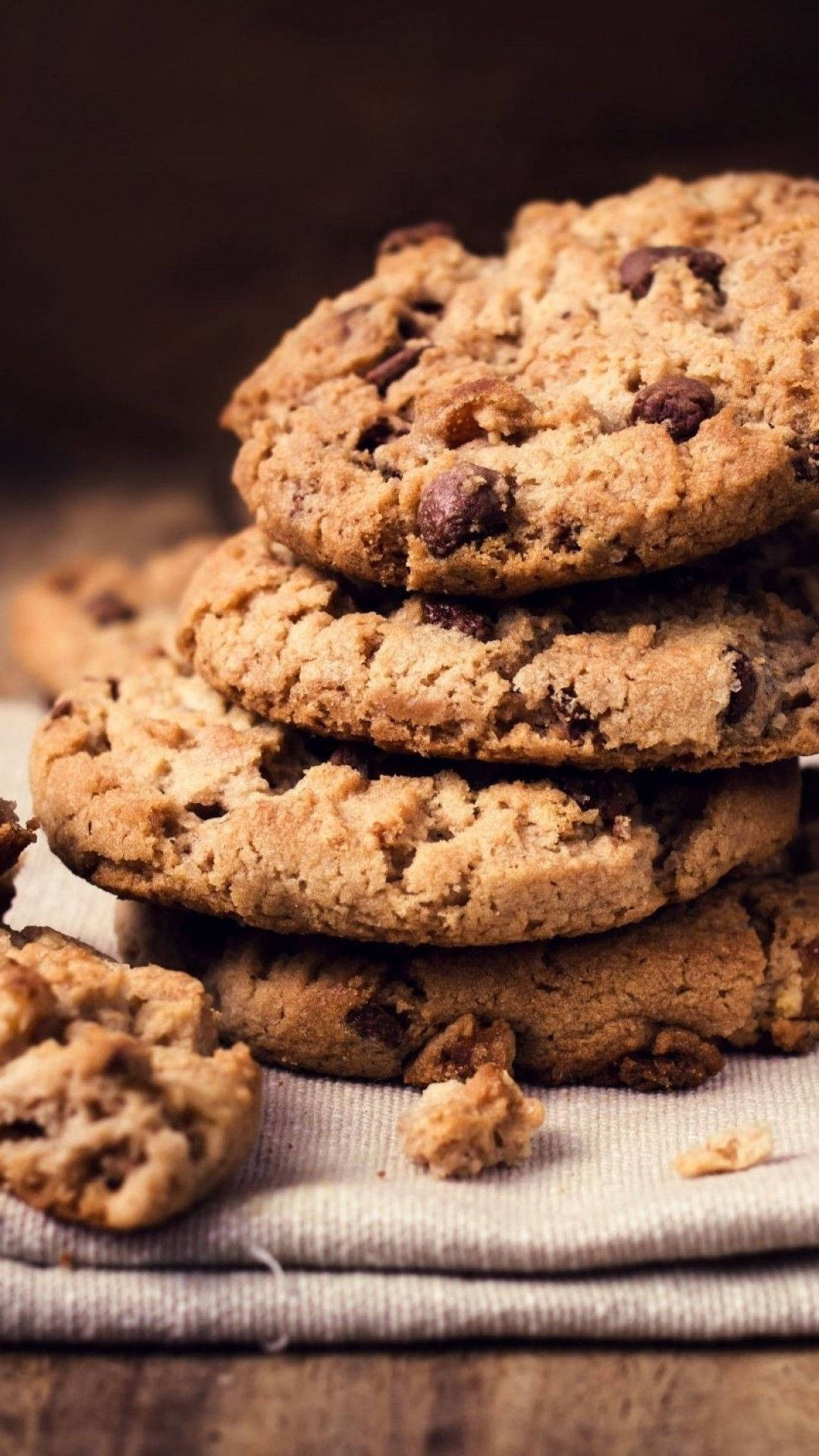 Cookies 桌布 壁紙 — 一堆溫暖的金色巧克力餅乾，帶有融化的巧克力塊，放在木質表面的亞麻布上。