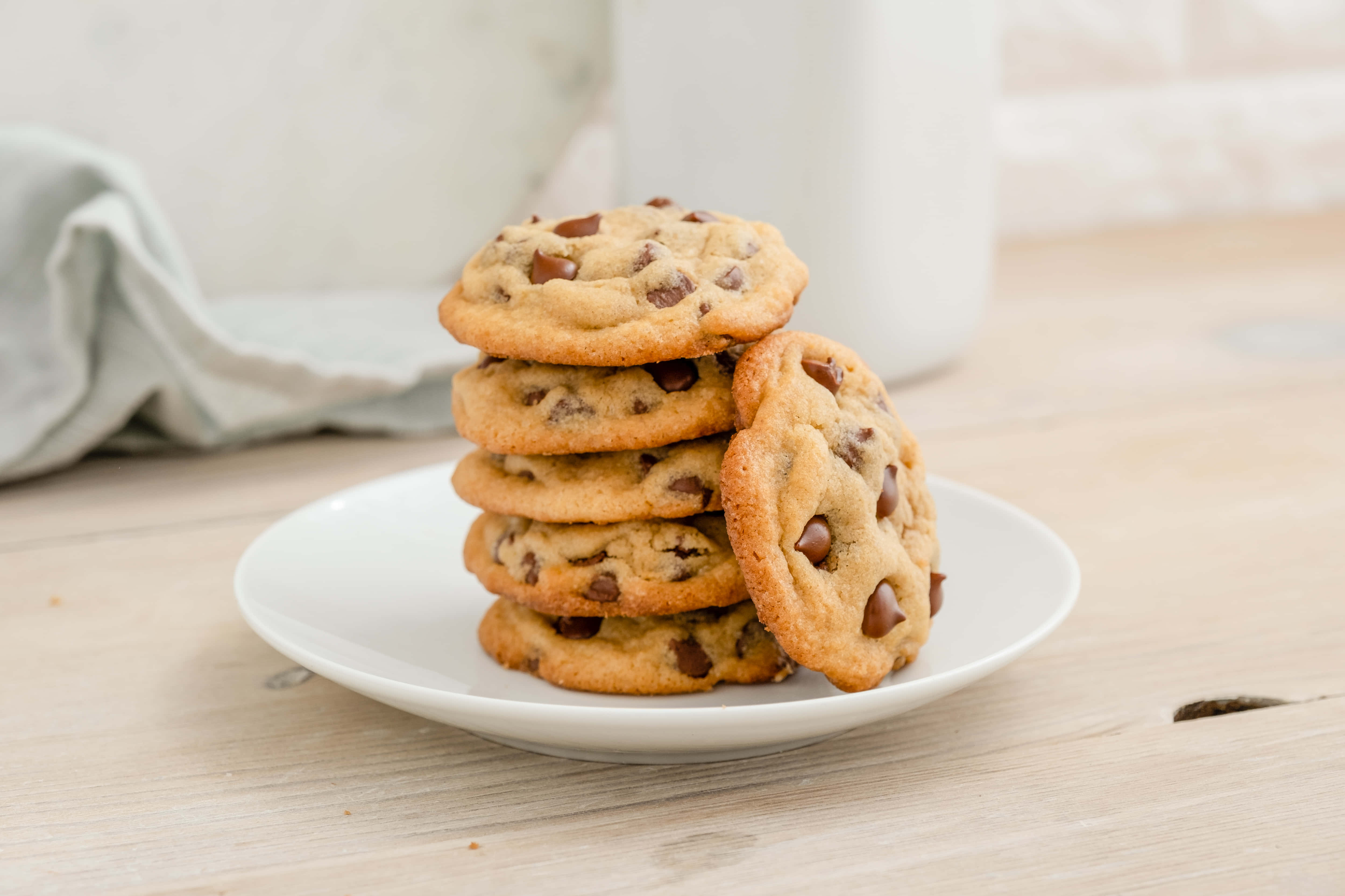Cookie 桌布 壁紙 — 一堆溫暖的金色巧克力餅乾放在淺色木桌上的一個白色盤子上，看起來很誘人。