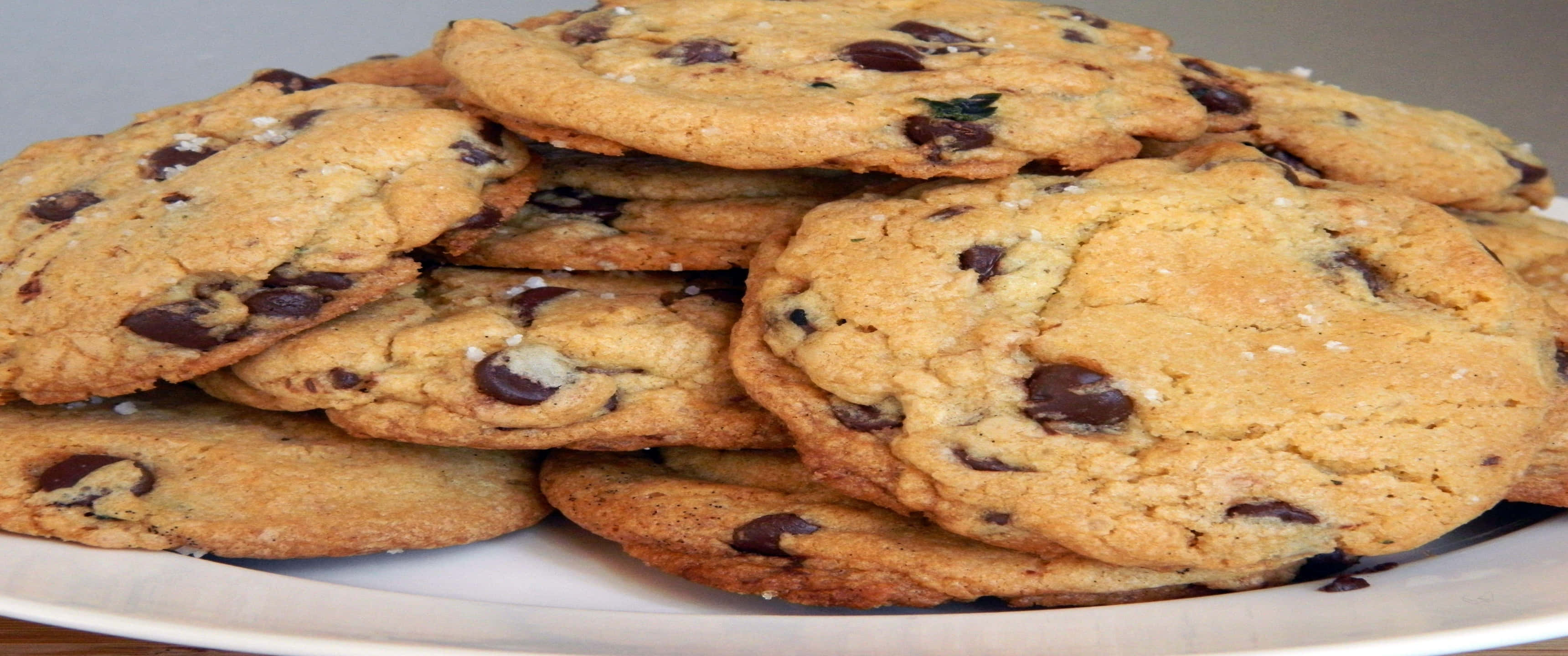 Cookies 桌布 壁紙 — 一堆溫暖金黃色的巧克力餅乾撒上海鹽，放在白色盤子上，令人垂涎。