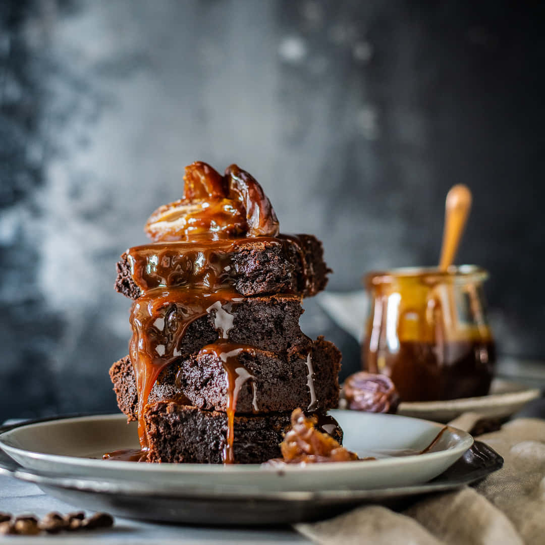 Caramel Brownie 桌布 壁紙 — 一堆濃郁的巧克力布朗尼，淋上閃亮的焦糖醬，並以焦糖化胡桃點綴。