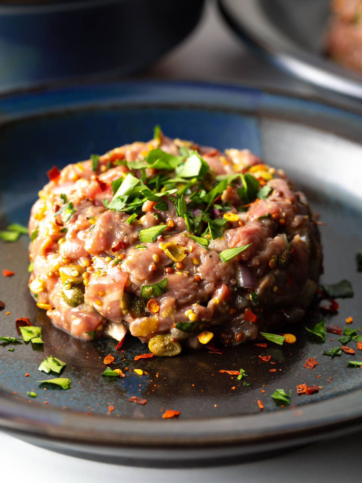 meat 桌布 壁紙 — 一堆生牛肉塔塔，配上新鮮香草和香料，放在深色陶瓷盤上。