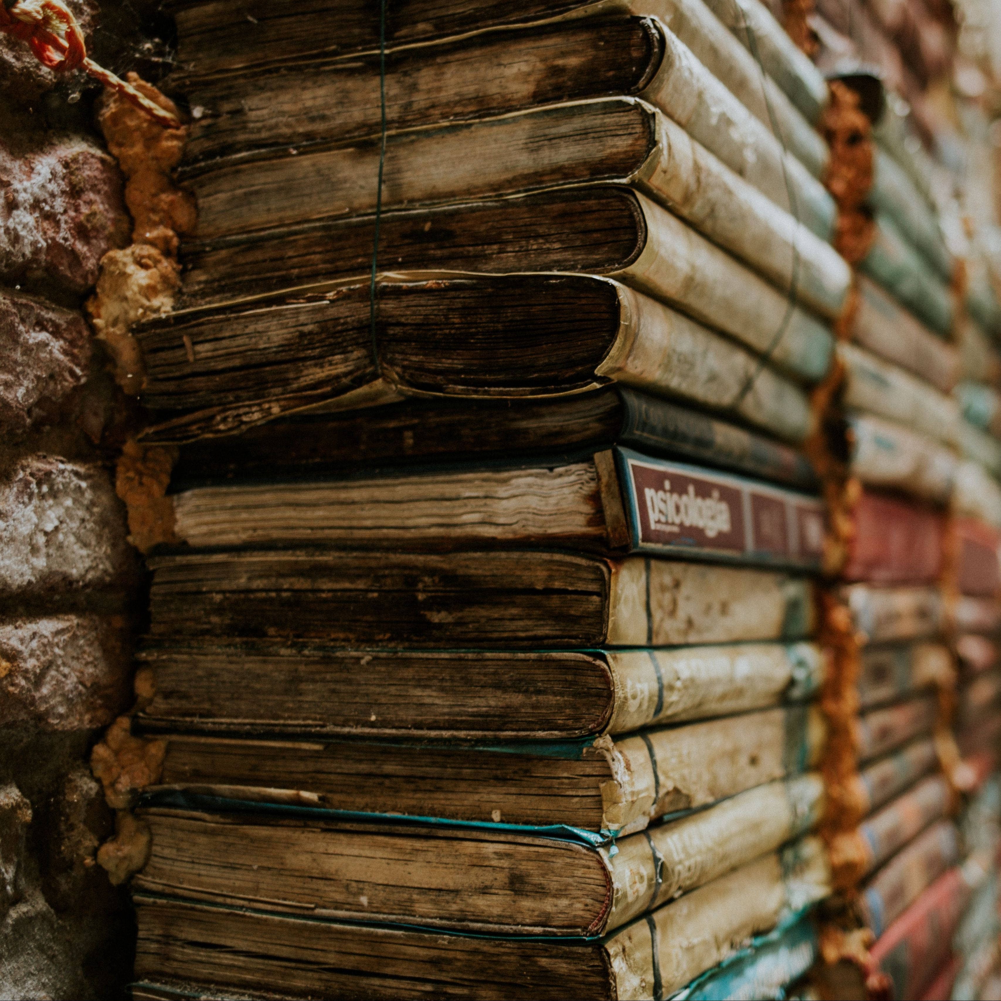 books 桌布 壁紙 — 一堆用麻繩捆綁的風化復古書籍，以溫暖的大地色調靠在一面破舊的磚牆上。