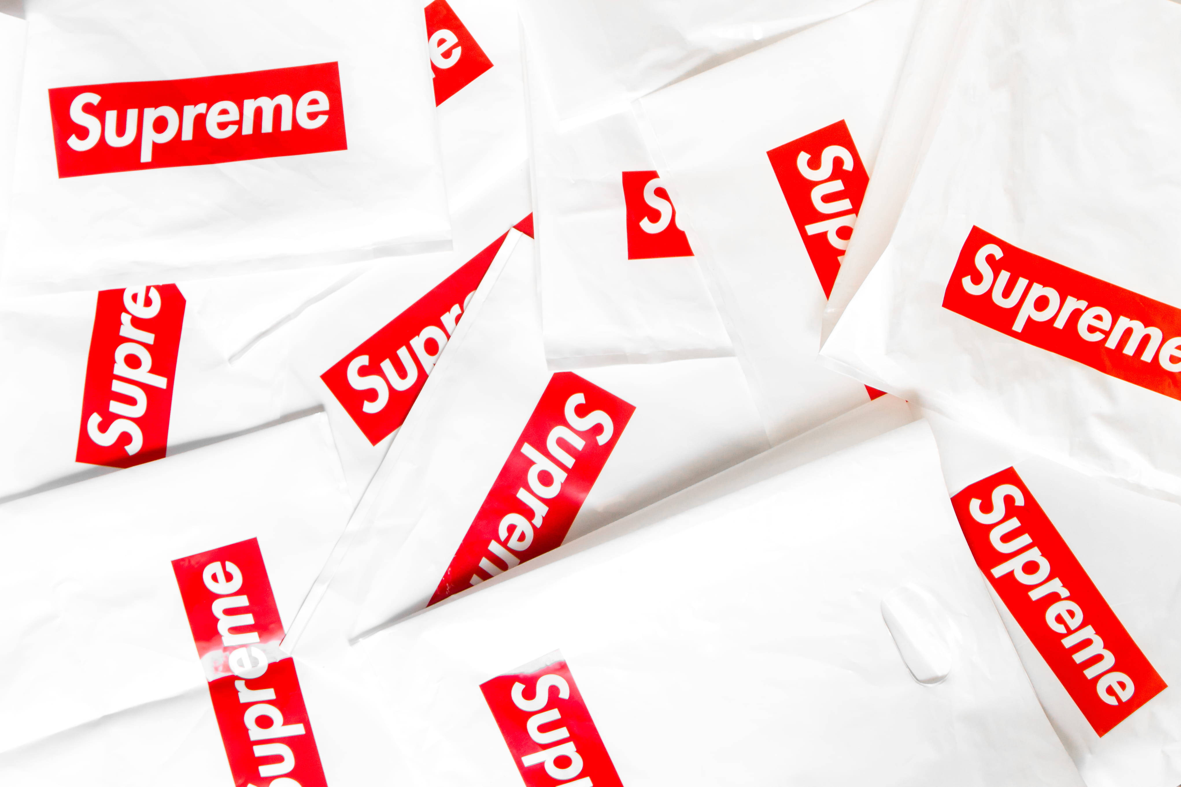 supreme 桌布 壁紙 — 一堆皺巴巴的白色Supreme購物袋，表面散落著大膽的紅色標誌。