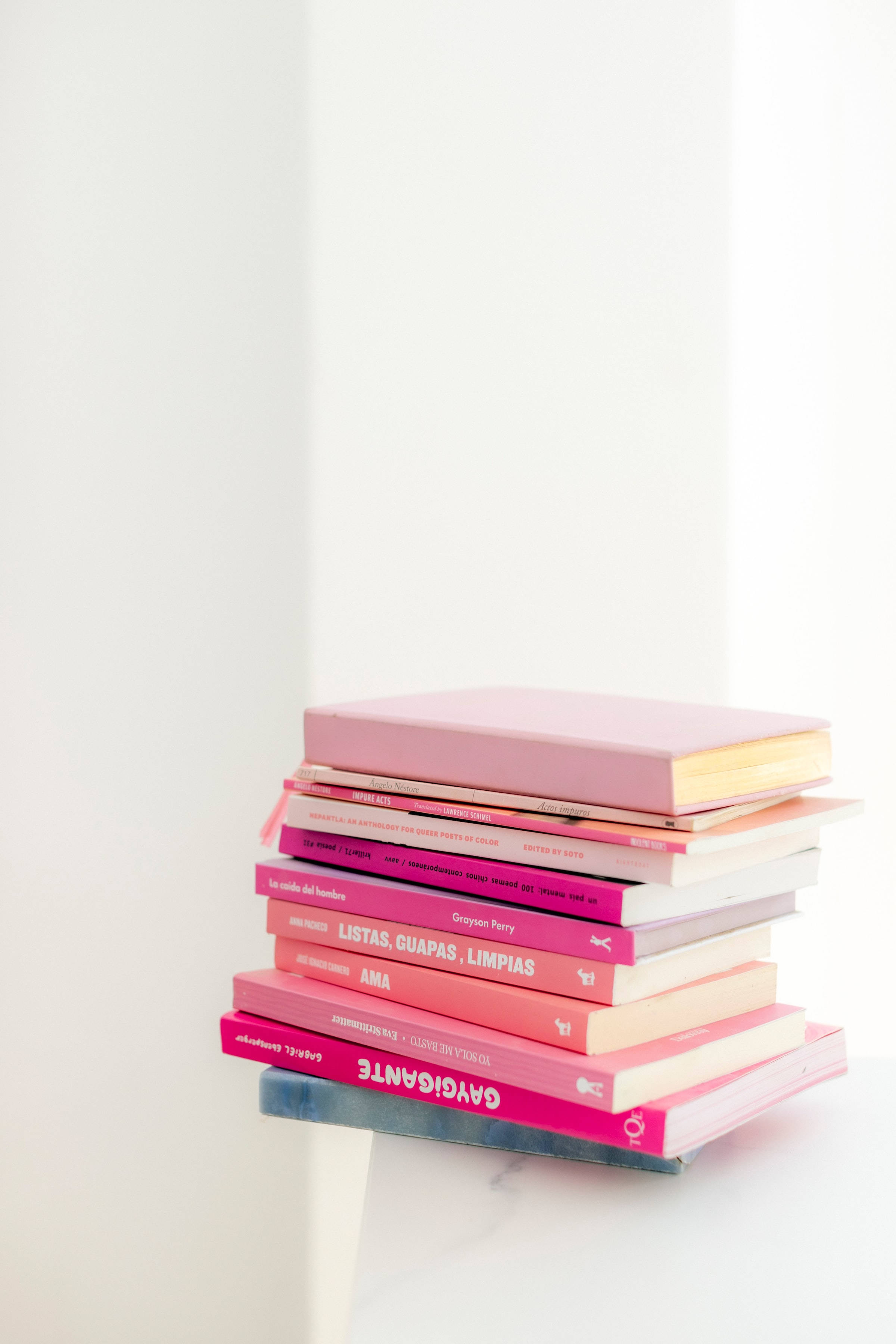 books 桌布 壁紙 — 一堆粉紅色和珊瑚色的書整整齊齊地放在大理石表面上，背景是明亮的白色牆壁。