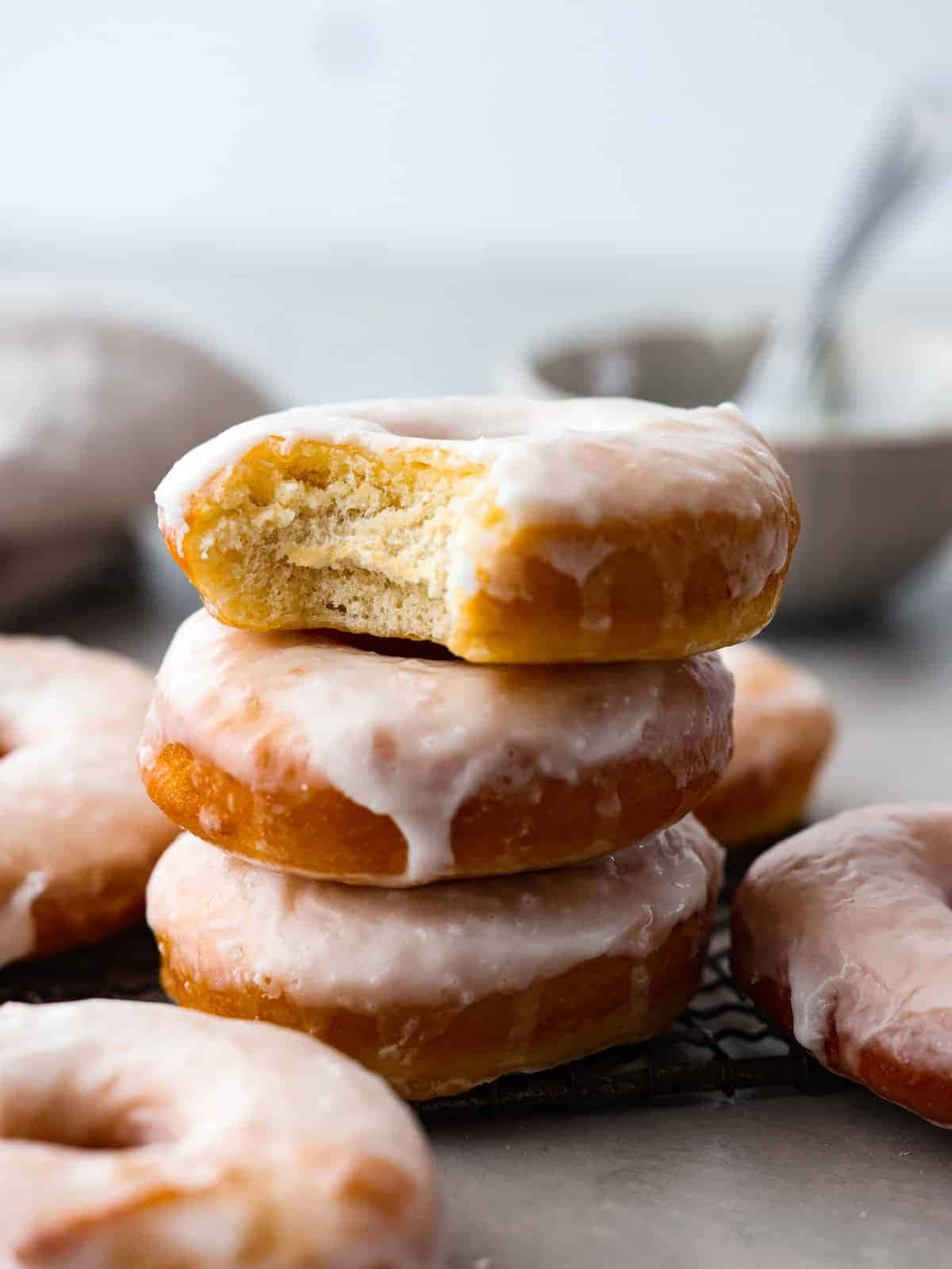 Glazed Donut 桌布 壁紙 — 一堆糖霜甜甜圈，其中一個被咬了一口，露出柔軟蓬鬆的內部，放在冷卻架上。