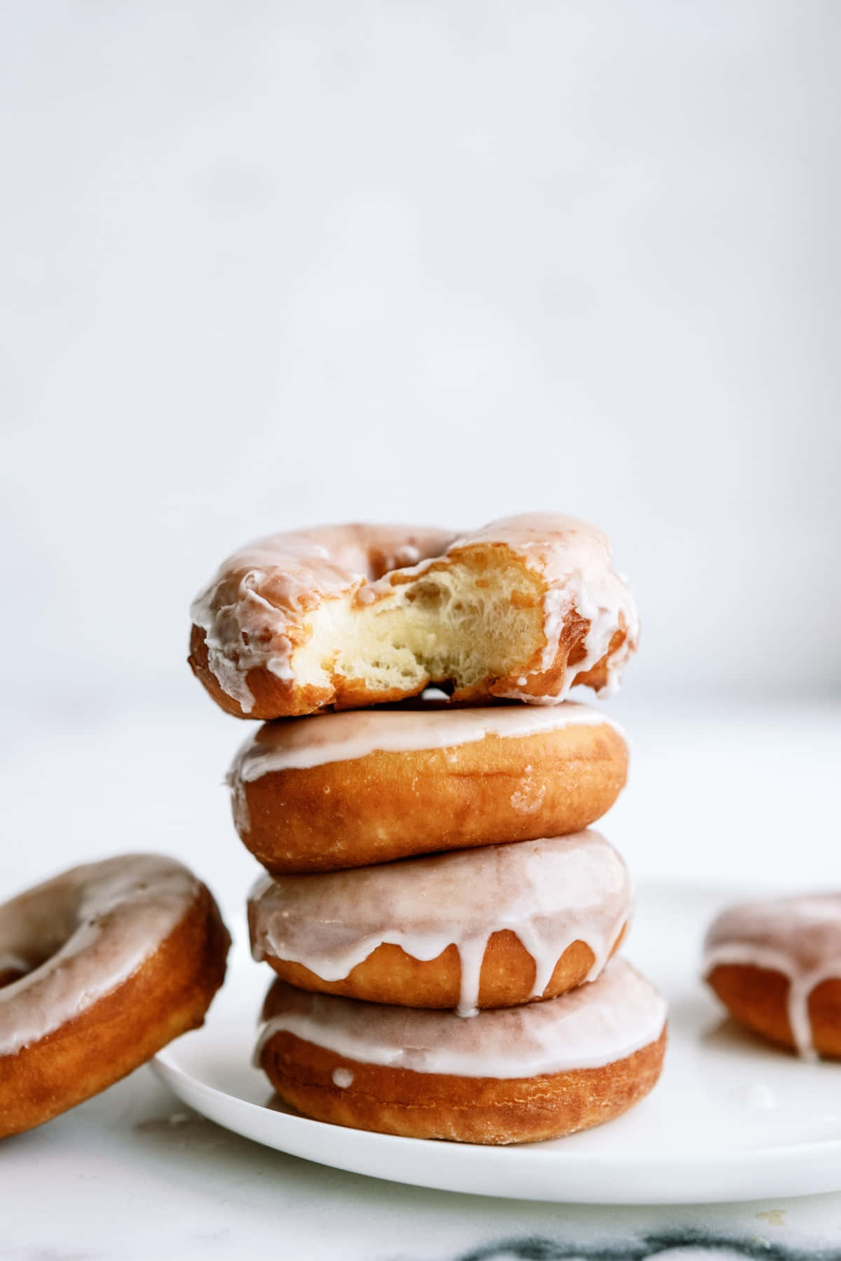Glazed Donut 桌布 壁紙 — 一堆糖霜甜甜圈，其中一個被咬了一口，露出柔軟蓬鬆的內部，背景是明亮的白色。