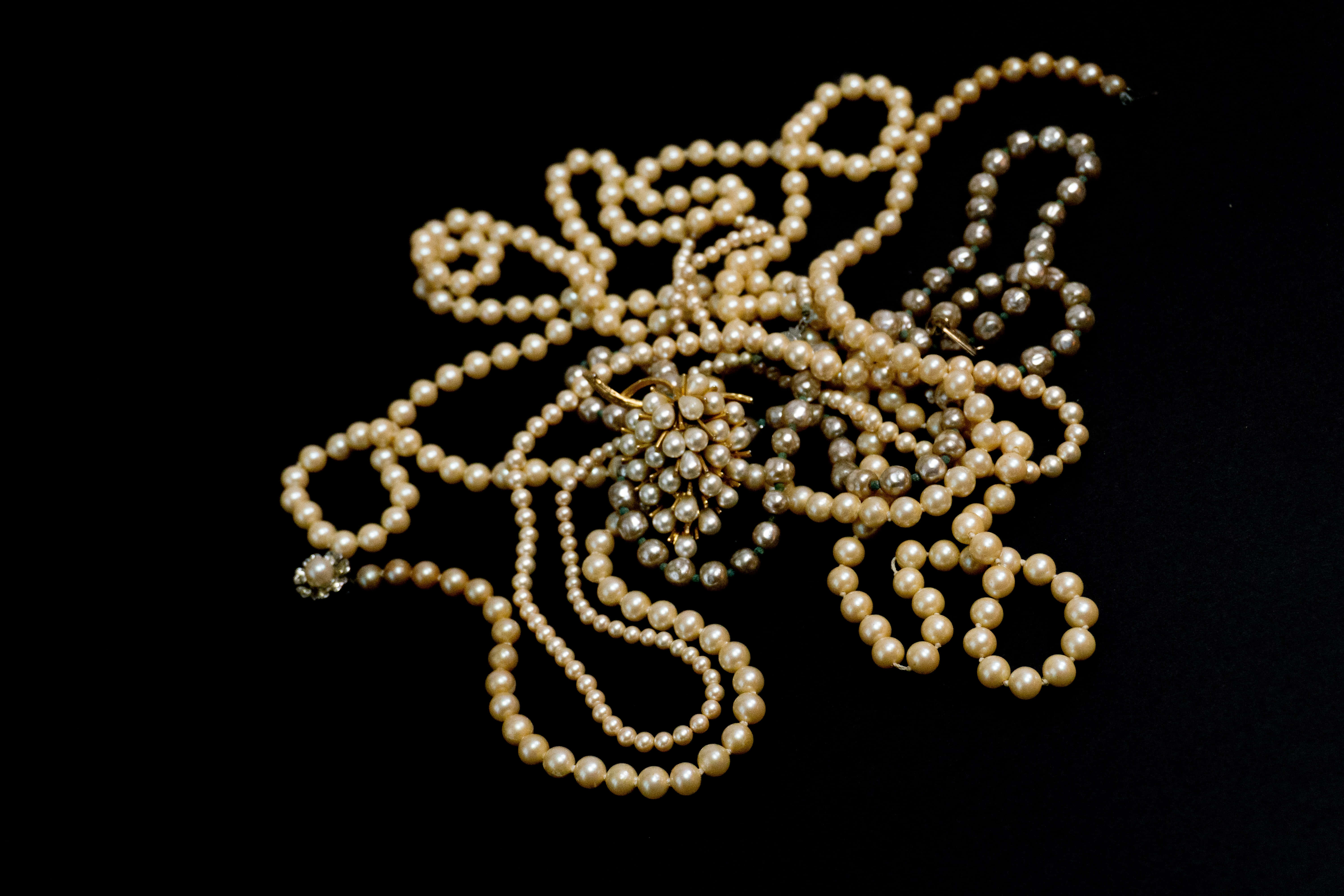 pearl 桌布 壁紙 — 一堆纏繞的奶油色和銀色珍珠，搭配金色胸針，在純黑背景上呈現。