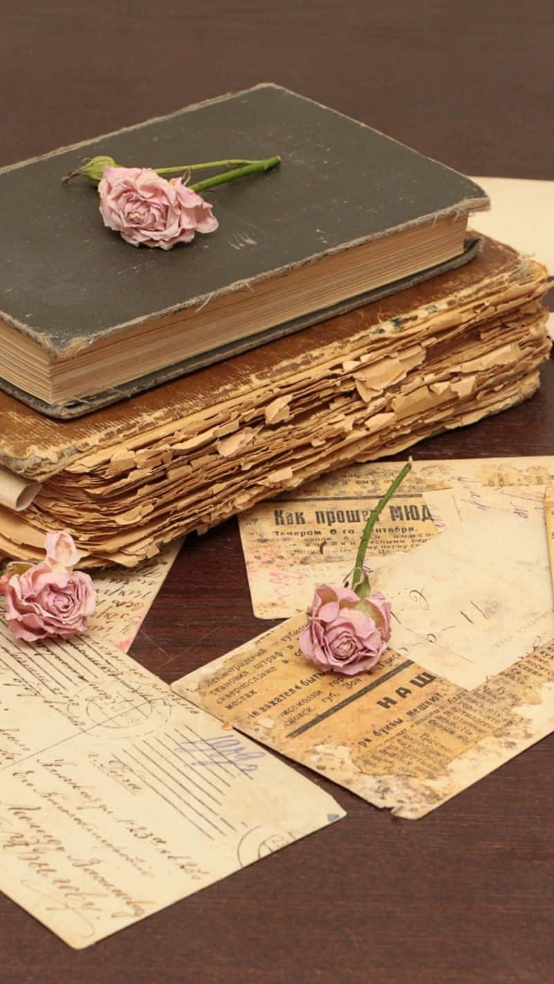 books 桌布 壁紙 — 一堆舊書和泛黃的信件，點綴著精緻的粉紅玫瑰，放在深色木質表面上。