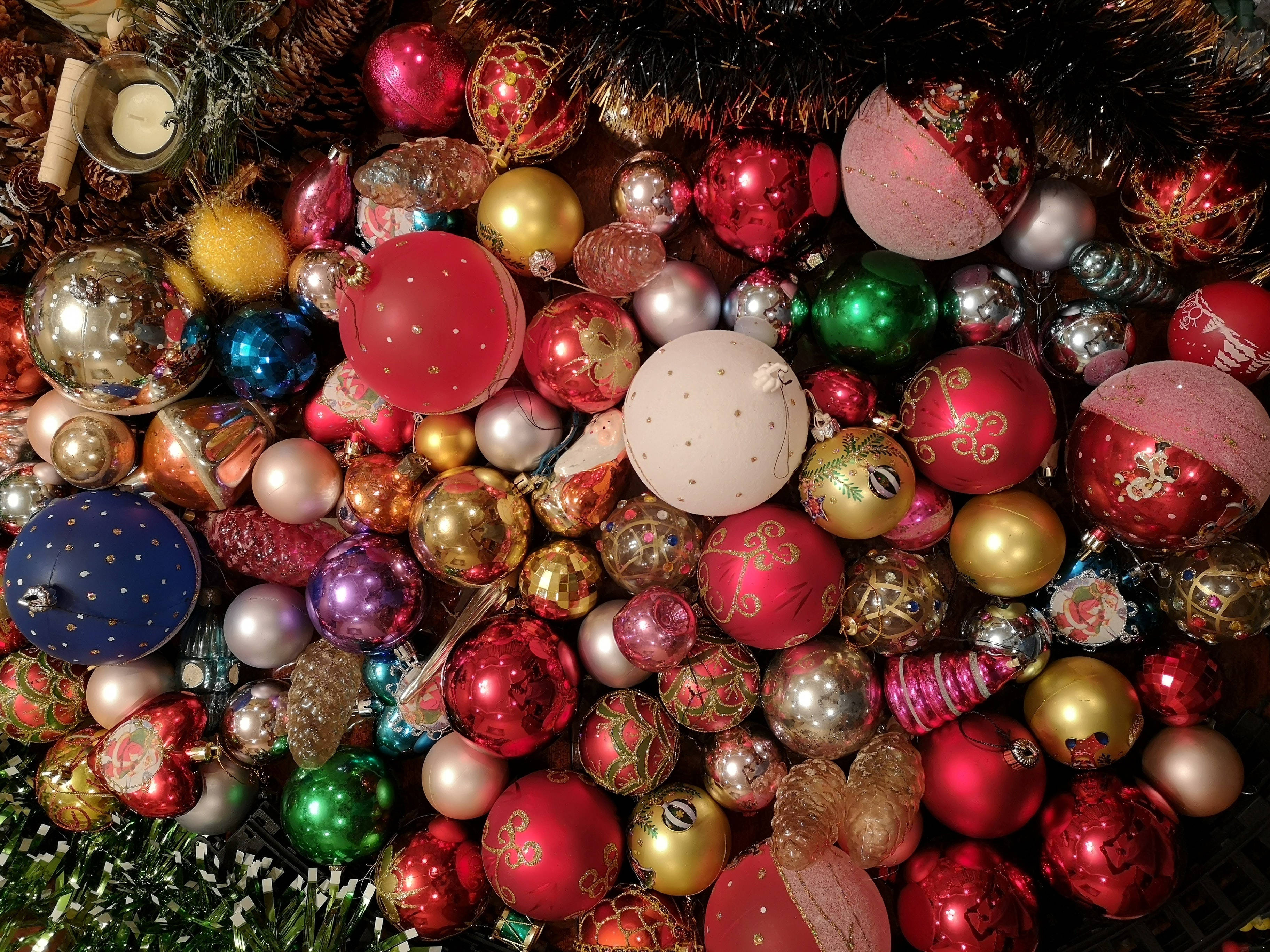 balls 桌布 壁紙 — 一堆色彩繽紛、閃閃發光的聖誕裝飾品，有紅色、金色和綠色，夾雜在亮片和松果之間。