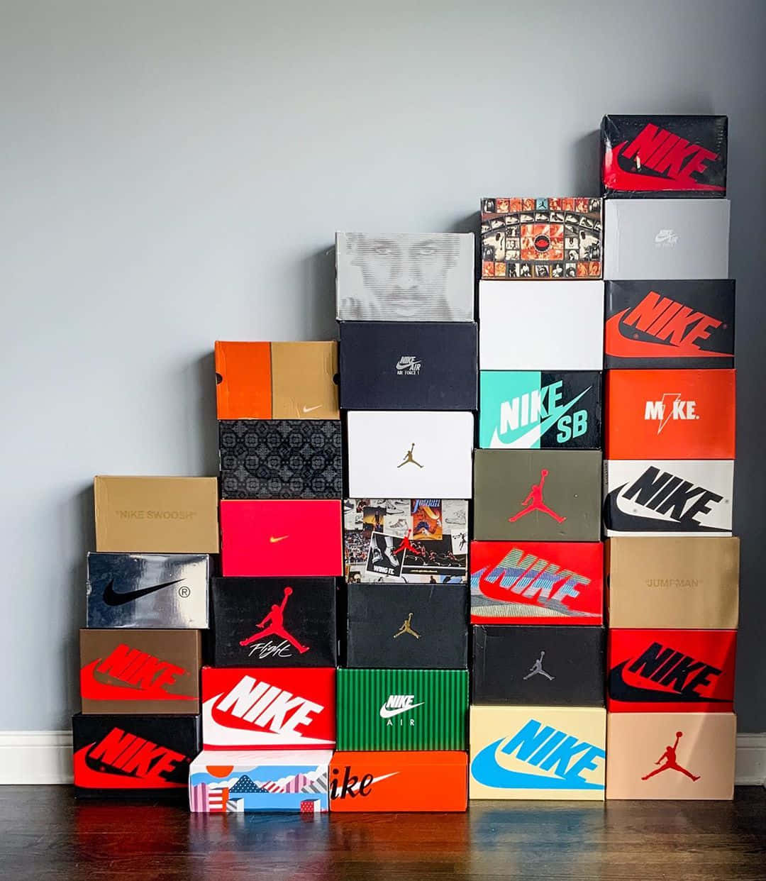 Shoe Box 桌布 壁紙 — 一堆色彩繽紛的Nike和Jordan運動鞋盒，排列在深色木地板上的一面素牆前。
