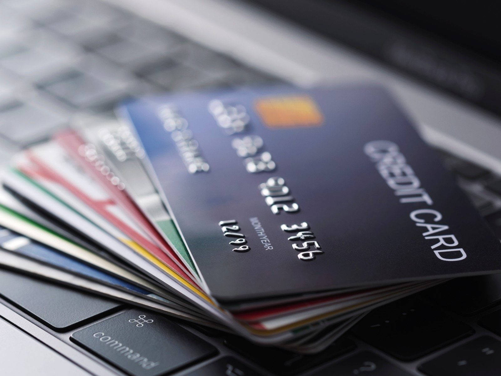Credit Card 桌布 壁紙 — 一堆色彩繽紛的信用卡以扇形排列，放在淺景深的筆記型電腦鍵盤上。