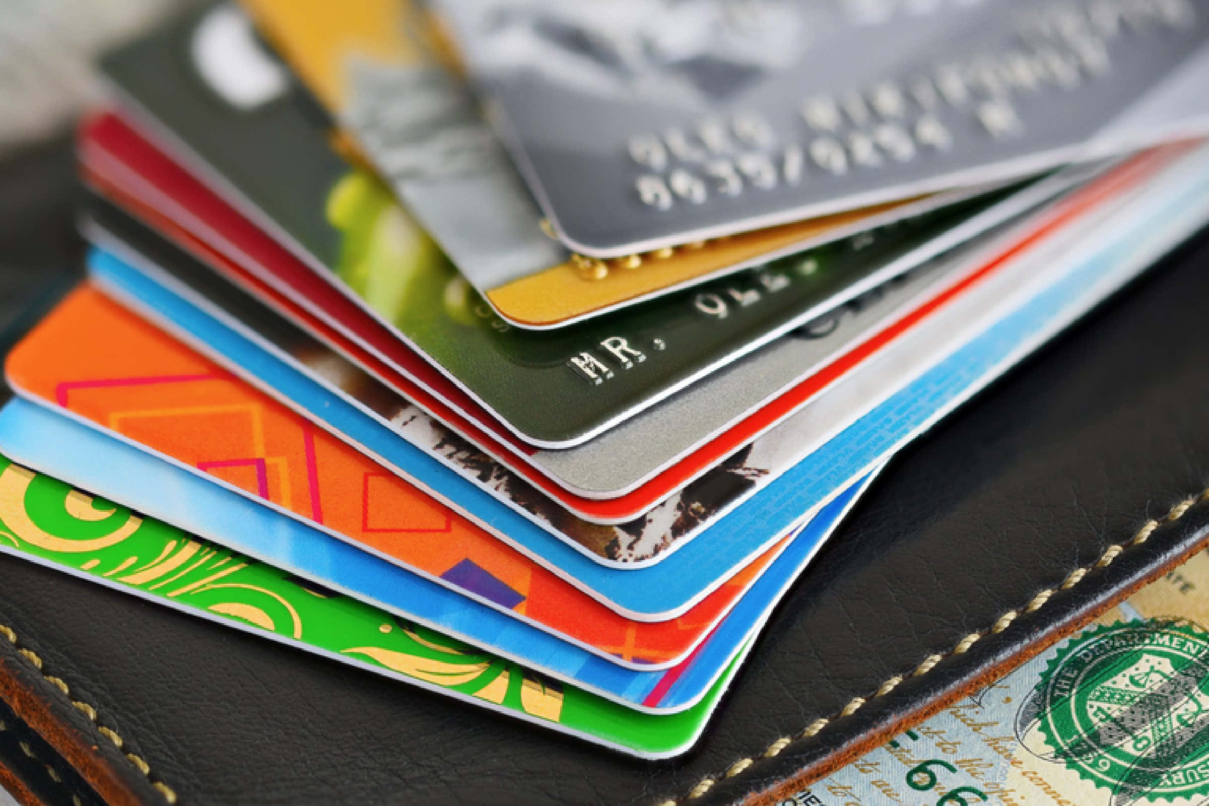 Credit Card 桌布 壁紙 — 一堆色彩繽紛的信用卡從黑色皮革錢包中扇形展開，縫線清晰可見。