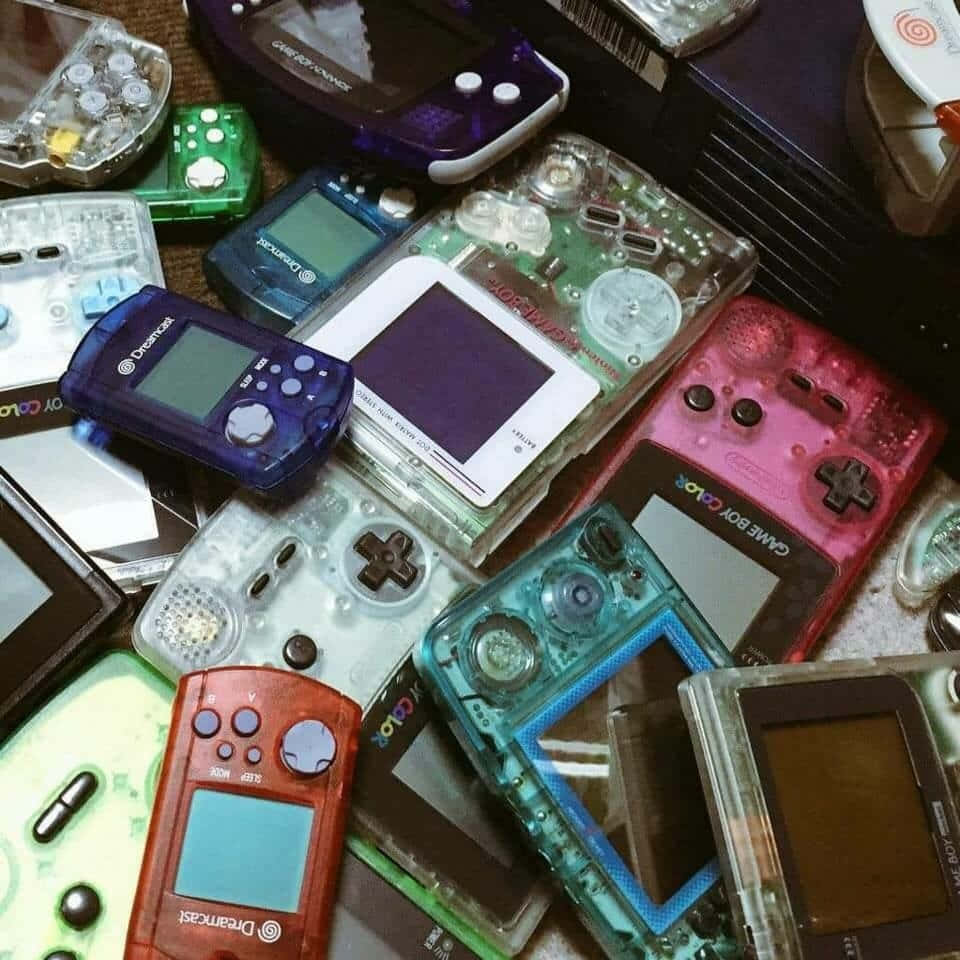 games 桌布 壁紙 — 一堆色彩繽紛的復古掌上型遊戲機，包括Game Boy Color和Dreamcast型號，散落在懷舊的堆中。
