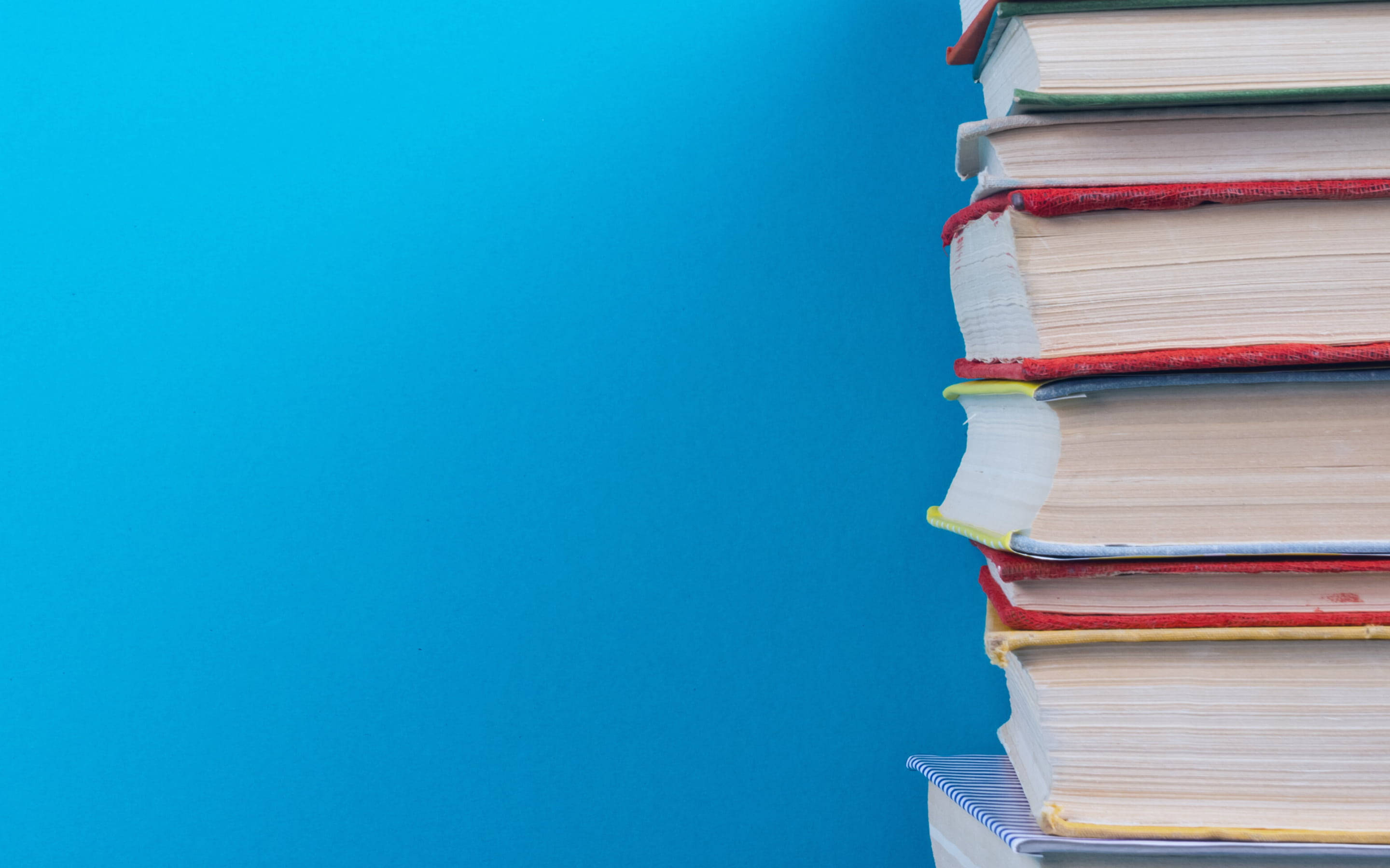 書本 桌布 壁紙 — 一堆色彩繽紛的書本高聳在純藍色背景上，並留有複製空間。