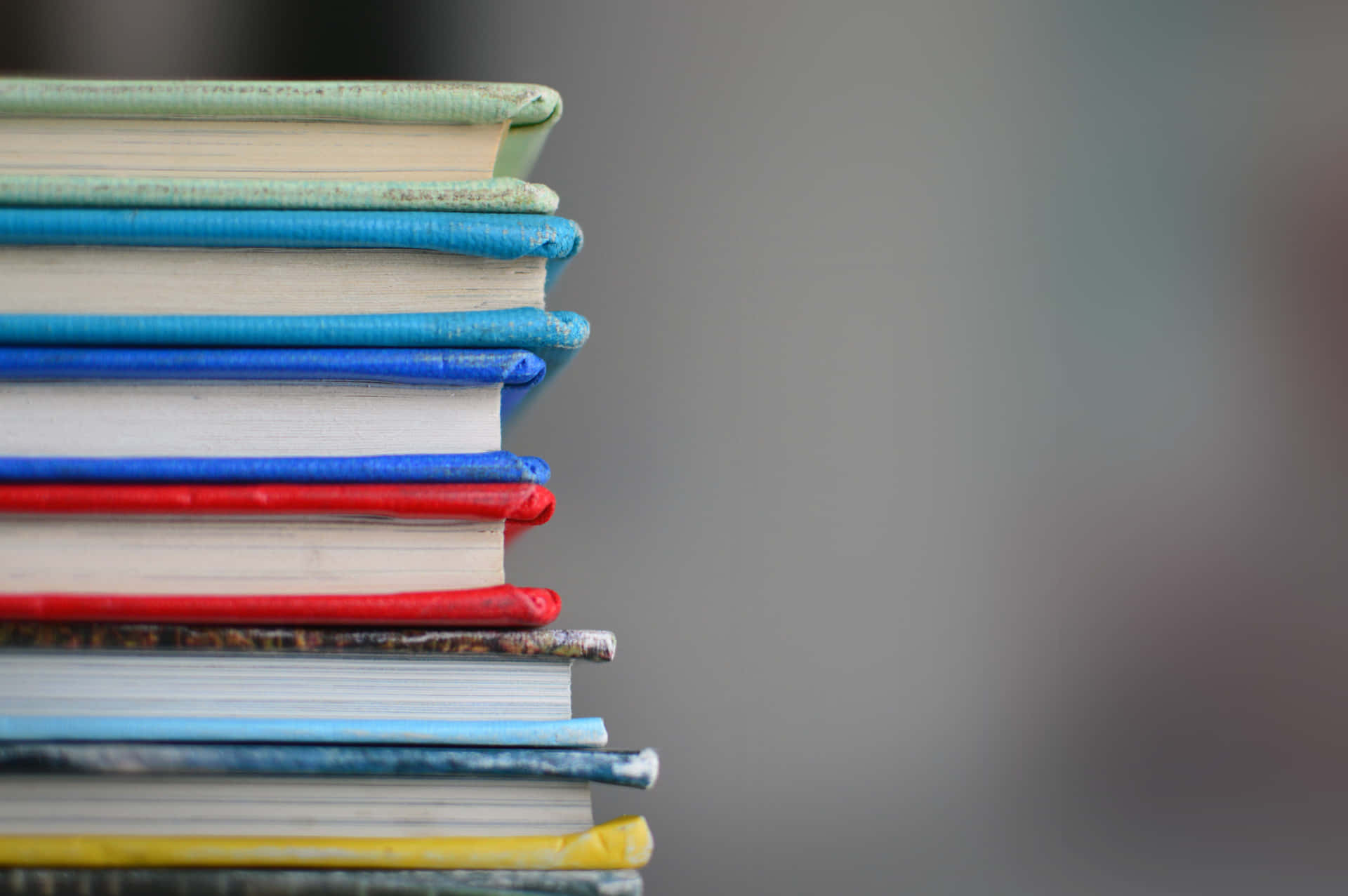Educated 桌布 壁紙 — 一堆色彩繽紛的書籍特寫，書脊帶有紋理，背景柔和模糊。
