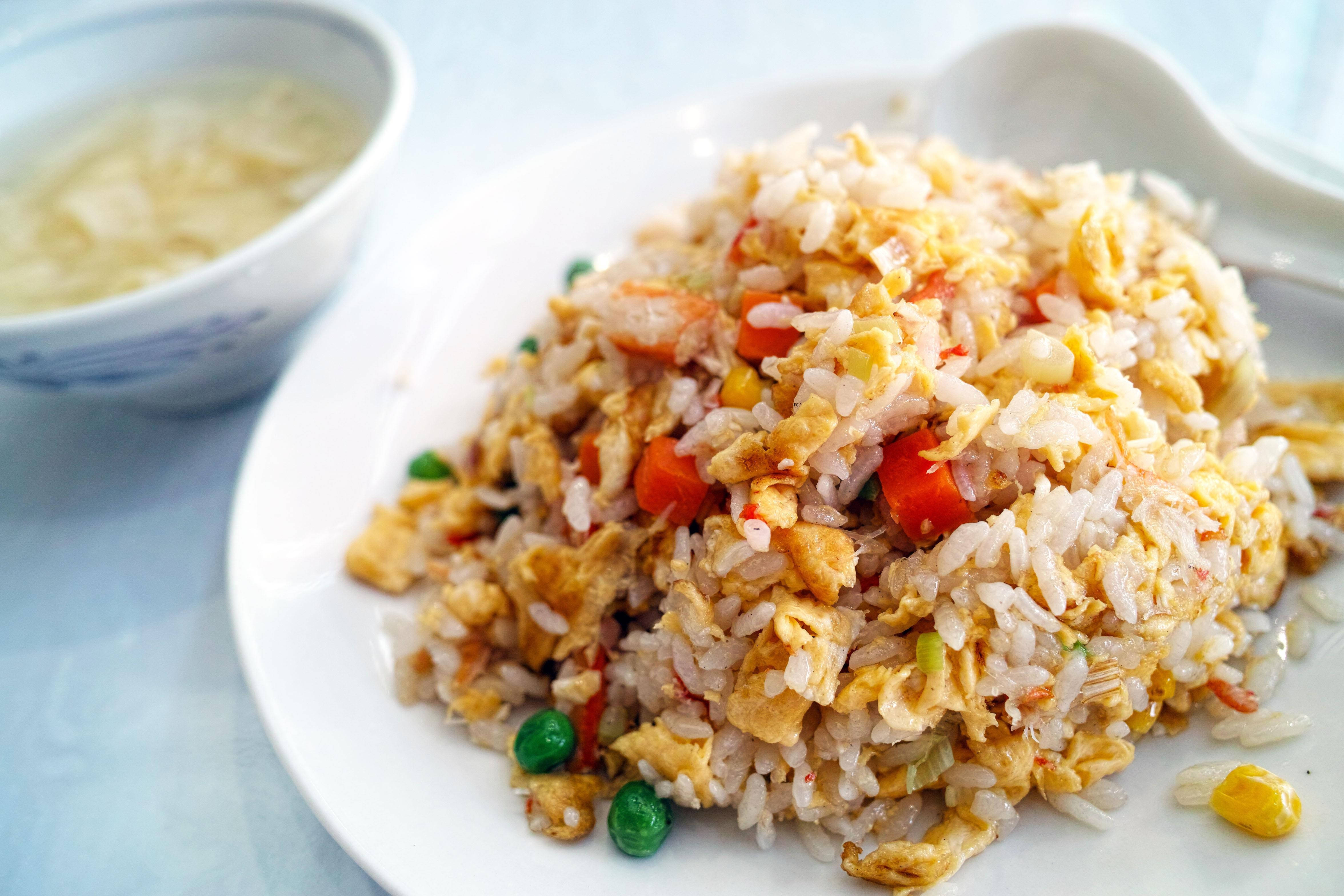 食物動圖 桌布 壁紙 — 一堆色彩繽紛的炒飯，配有雞蛋、紅蘿蔔和青豆，放在白色盤子上，旁邊有一碗湯。