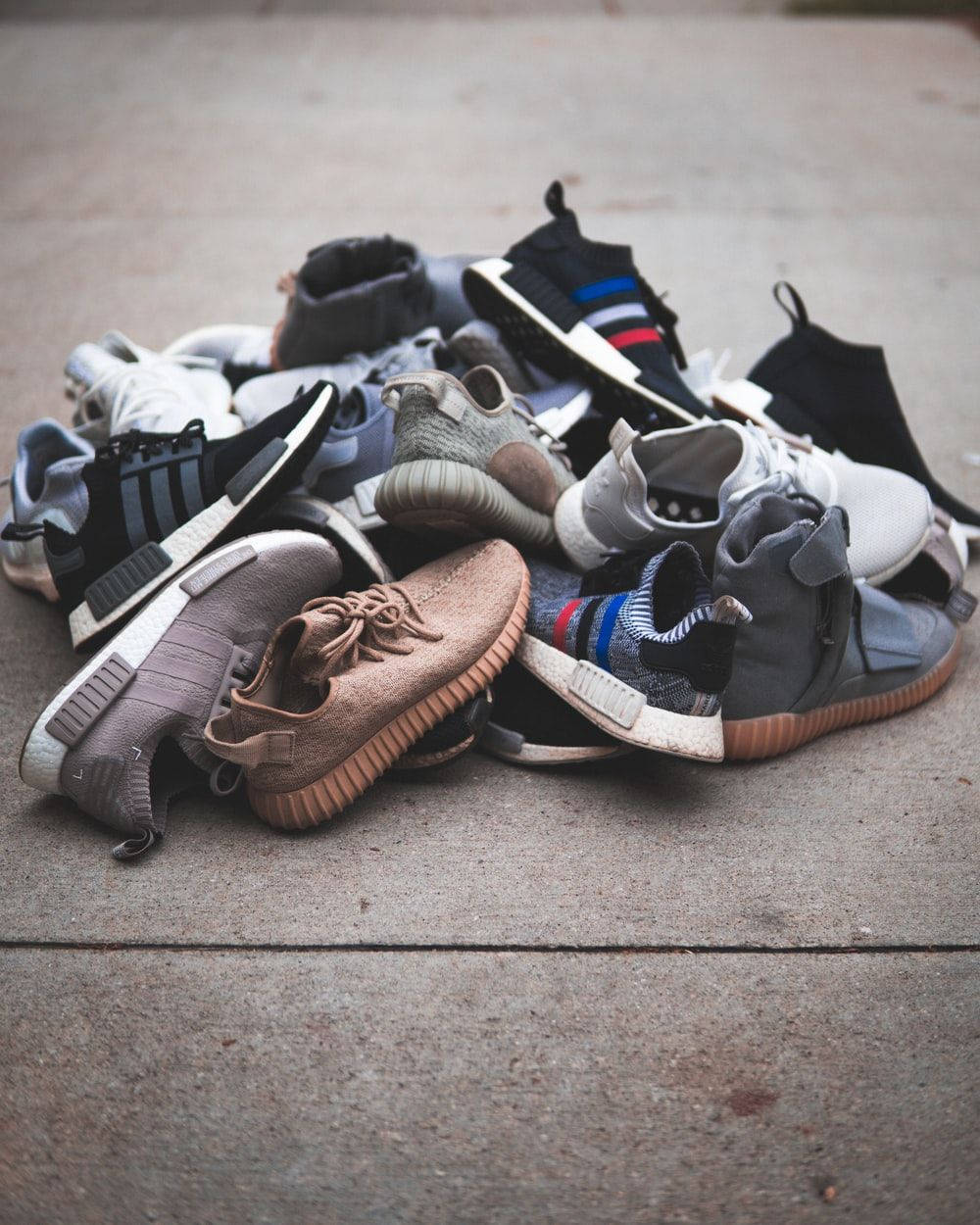 Sneaker 桌布 壁紙 — 一堆色彩繽紛的現代運動鞋散落在混凝土人行道上，柔和日光下。