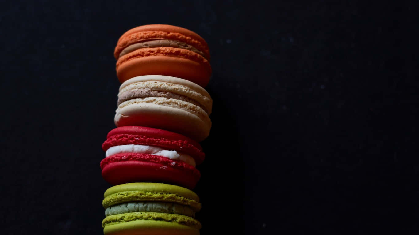 1366x768 Pastries 桌布 壁紙 — 一堆色彩繽紛的馬卡龍在深黑色背景下高高聳立，展現出細膩的質感和豐富的色調。