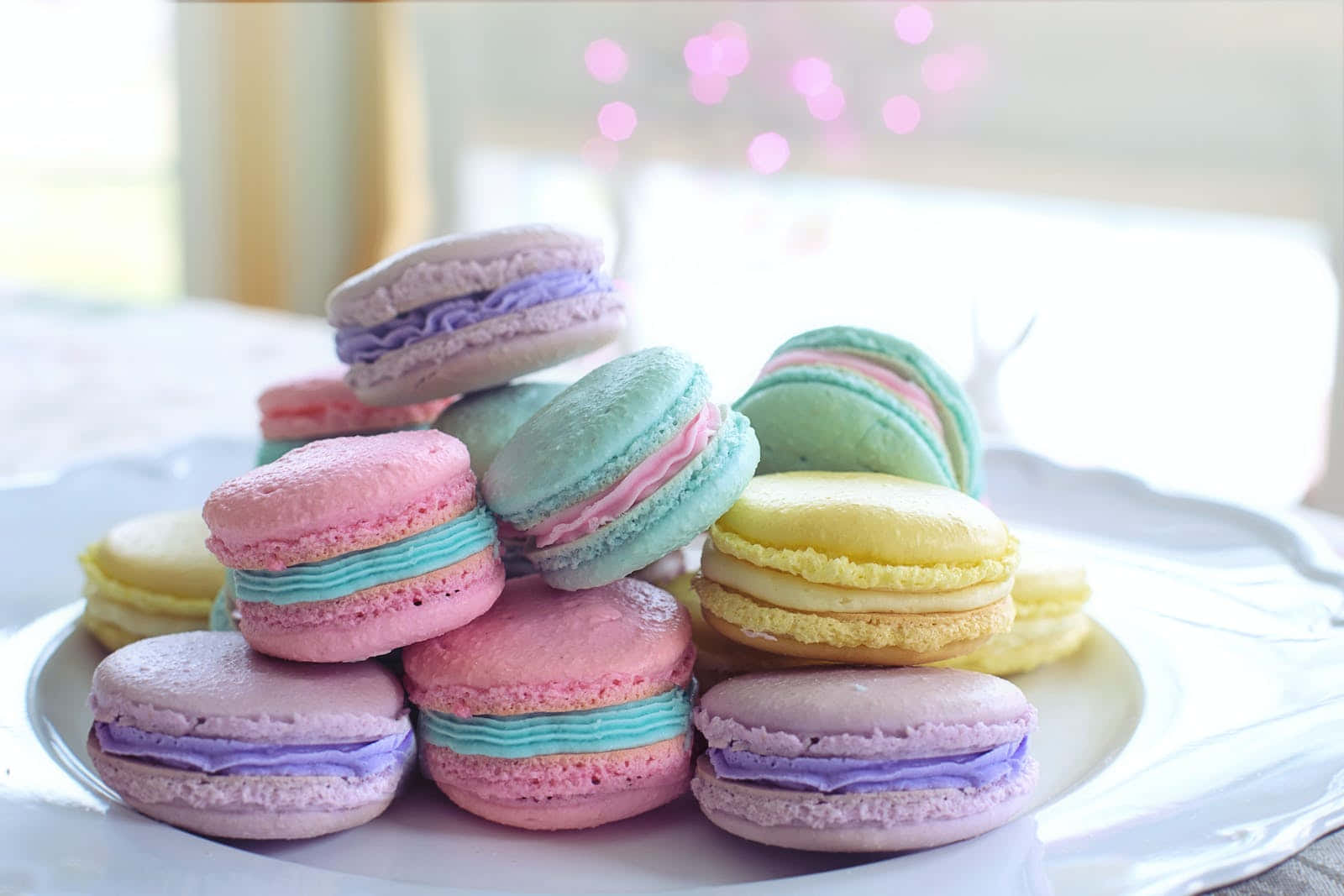 Pastel Easter 桌布 壁紙 — 一堆色彩繽紛的馬卡龍放在白色盤子上，旁邊有柔和的粉紅色散景燈光。
