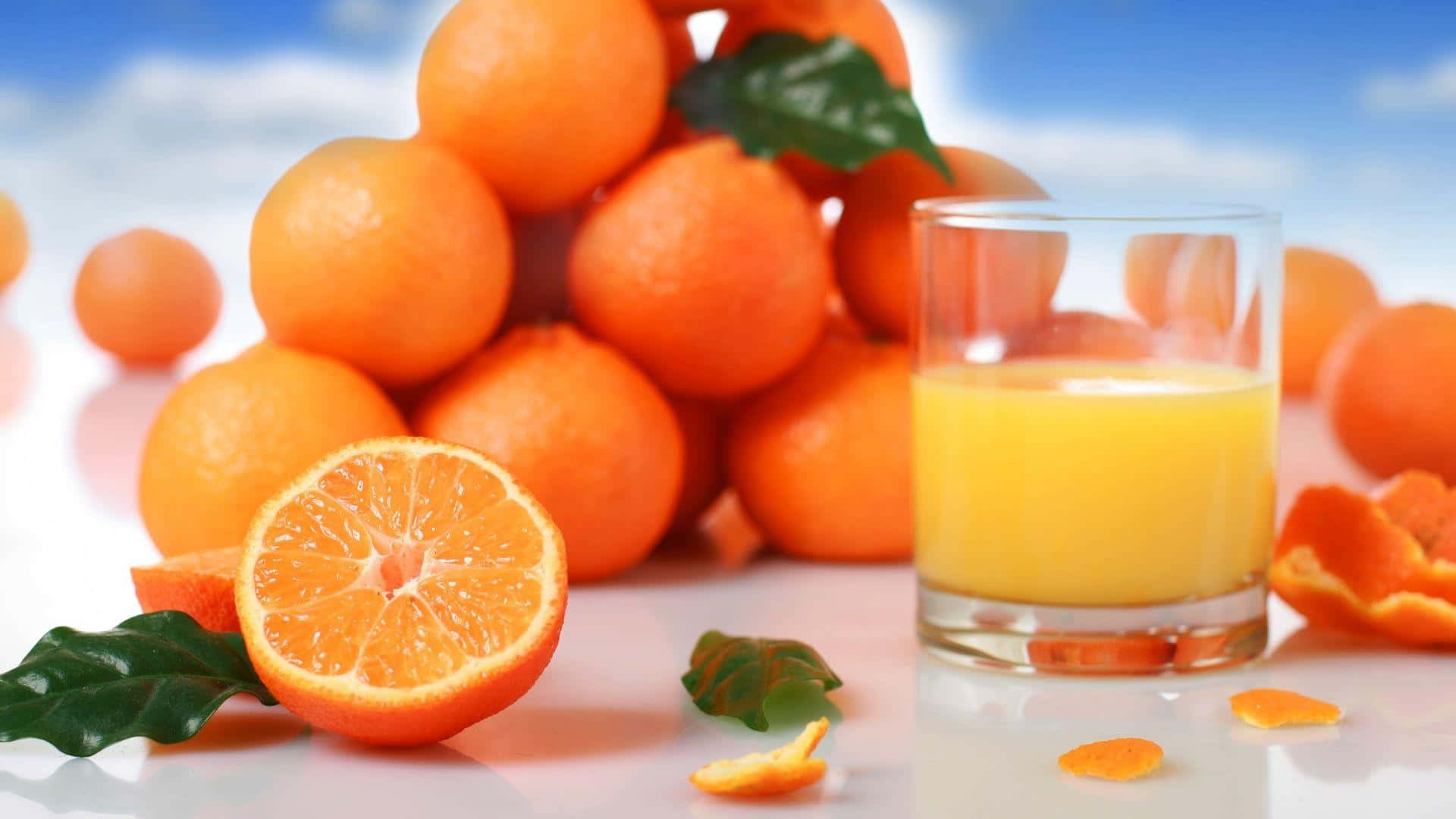 Orange Fruit 桌布 壁紙 — 一堆色彩鮮豔的完整和切片柳橙，配上一杯新鮮果汁，背景是明亮的藍天。