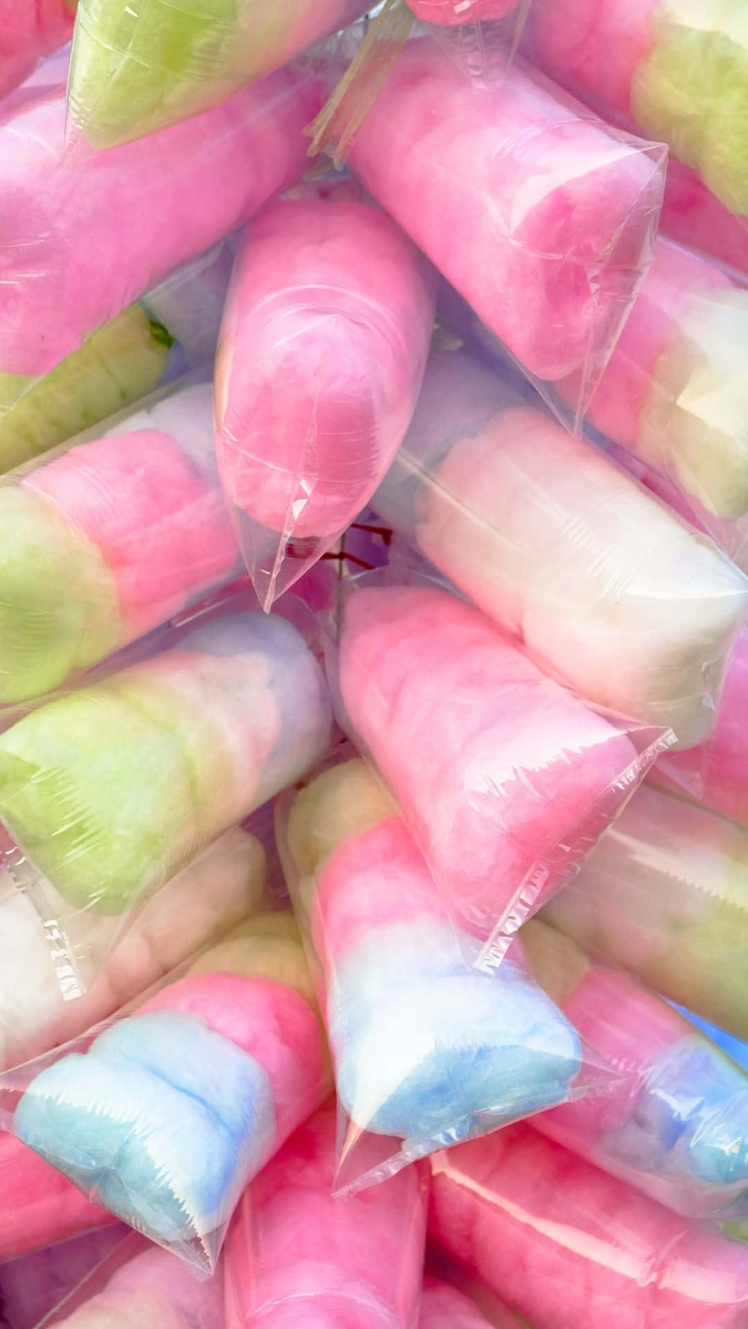 Cotton Candy 桌布 壁紙 — 一堆色彩鮮豔的獨立包裝棉花糖，呈現粉紅、綠色和藍色色調，在明亮光線下閃閃發光。