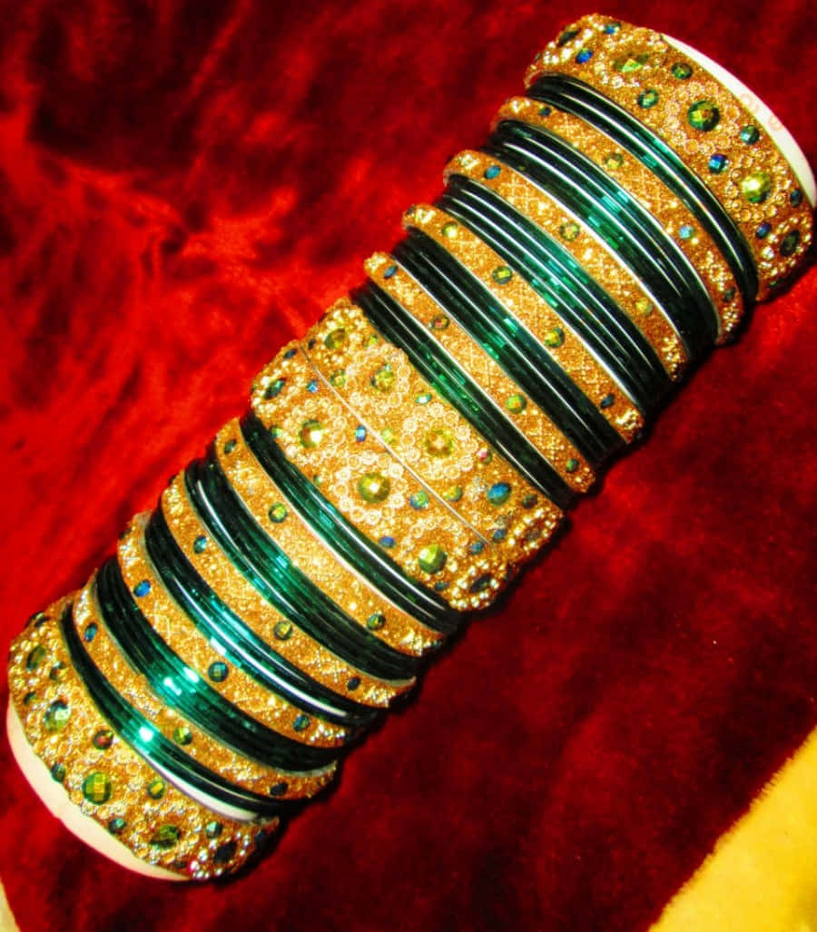 Bangles 桌布 壁紙 — 一堆華麗的金色和祖母綠手鐲，鑲嵌閃爍寶石，奢華地放在柔軟的紅色天鵝絨表面上。