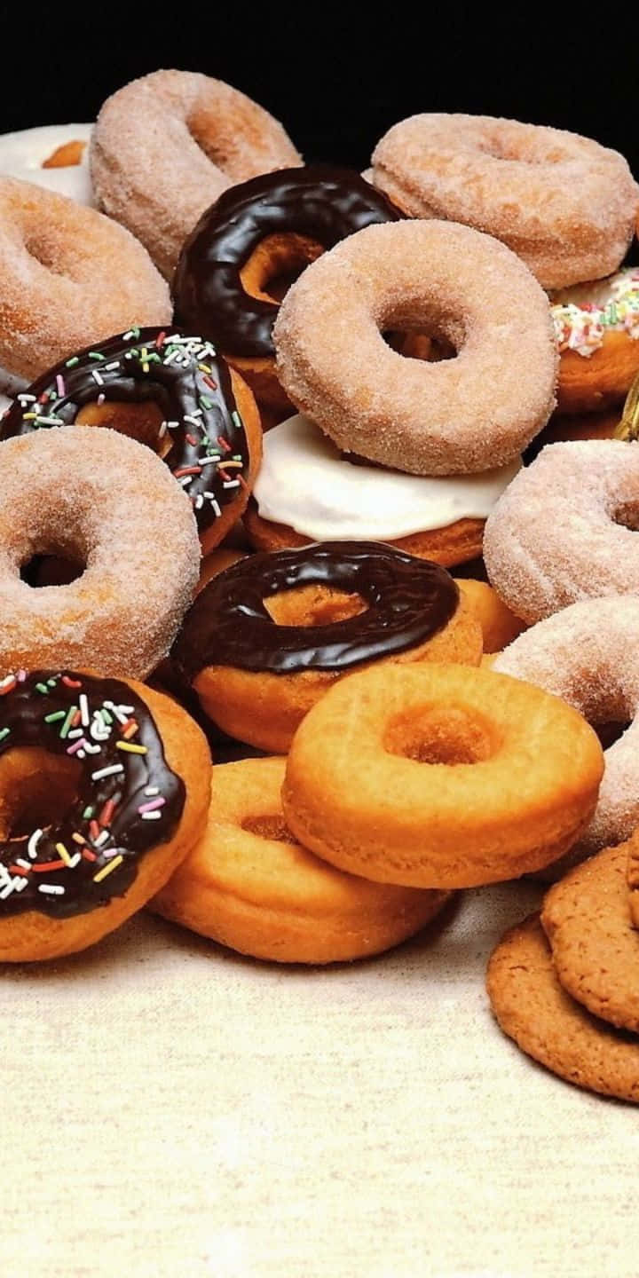 Pastry 桌布 壁紙 — 一堆誘人的各式巧克力糖霜、彩針和原味甜甜圈高高堆在淺色表面上。