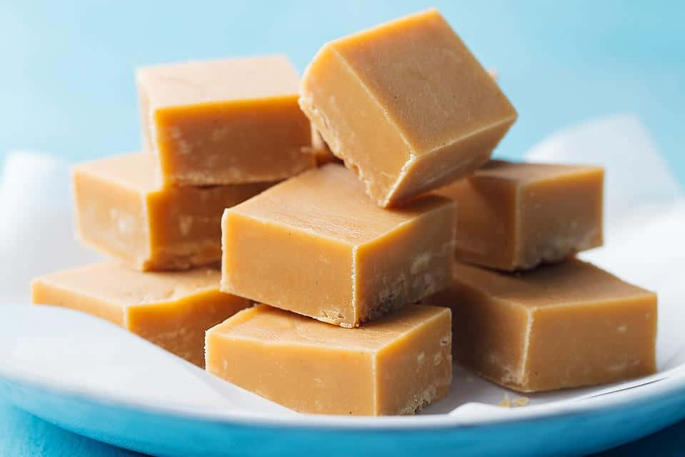 Penuche Fudge 桌布 壁紙 — 一堆誘人的金黃色焦糖方塊放在亮藍色盤子上，襯托著柔和的藍色背景。