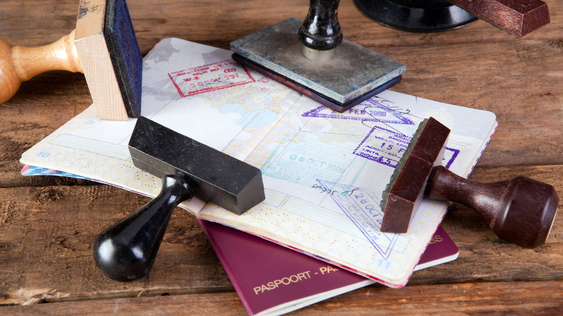 Passport 桌布 壁紙 — 一堆護照和旅行印章放在質樸的木桌上，喚起全球冒險和旅行慾望。