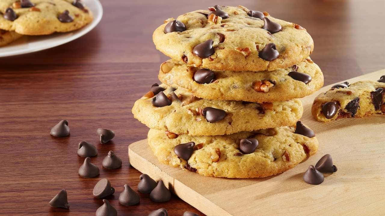 720p Cookies 桌布 壁紙 — 一堆金黃色巧克力餅乾加胡桃放在木砧板上，周圍散落巧克力碎片。
