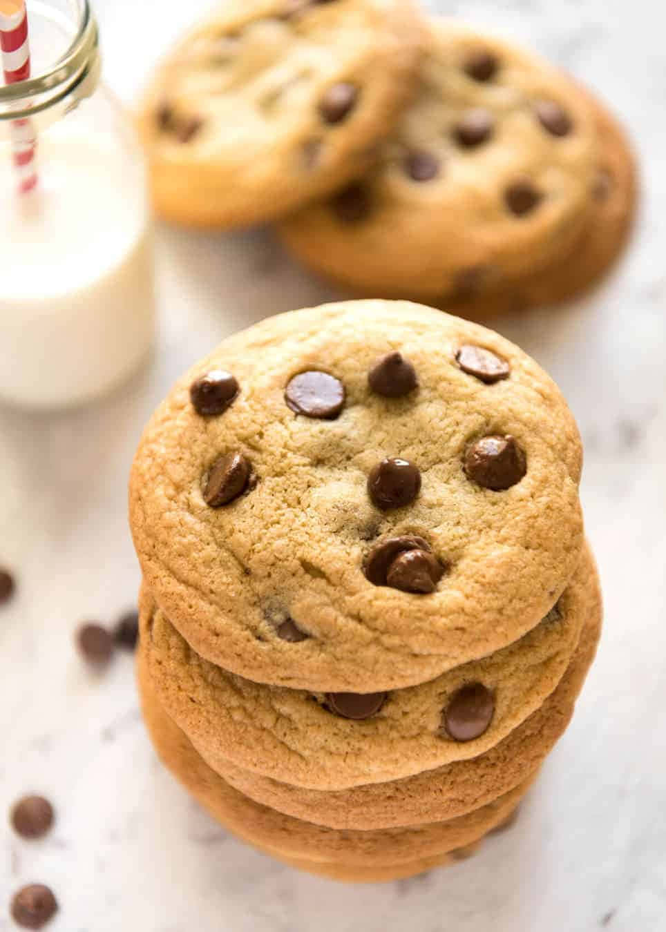 Cookie 桌布 壁紙 — 一堆金黃色的巧克力曲奇餅，旁邊放著一杯牛奶，牛奶杯裡插著一支紅白條紋的吸管。