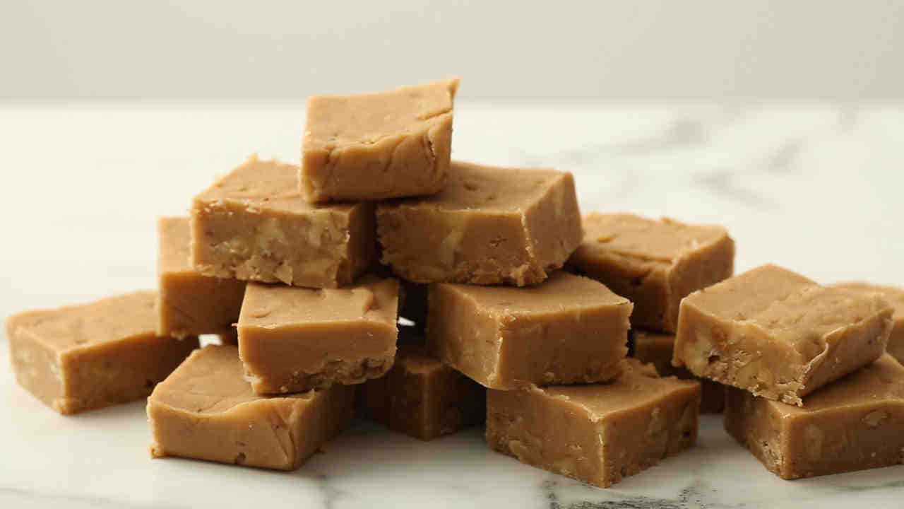 Penuche Fudge 桌布 壁紙 — 一堆金黃色的花生醬軟糖方塊放在乾淨的白色大理石表面上，令人垂涎。