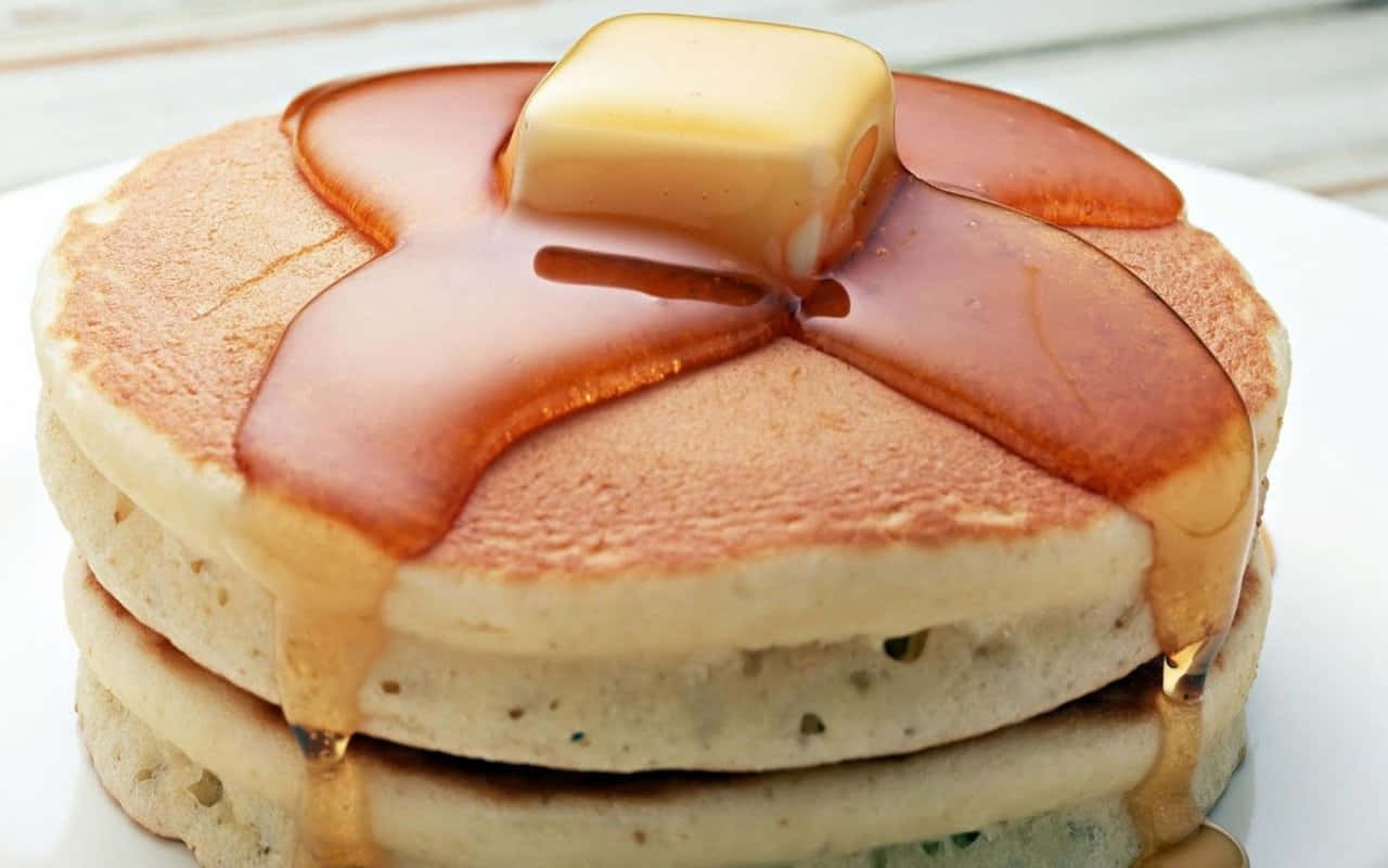 Butter 桌布 壁紙 — 一堆金黃色鬆餅，上面淋上閃亮的糖漿和一塊正在融化的奶油，放在白色盤子上。