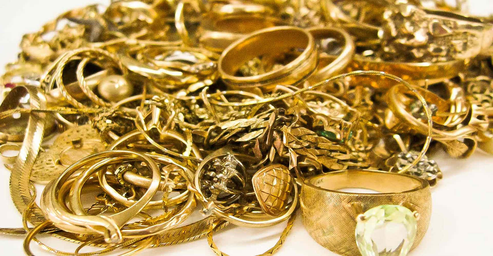 金色動態 桌布 壁紙 — 一堆閃閃發光的復古黃金首飾，包括戒指、鏈條和胸針，散落在白色表面上。