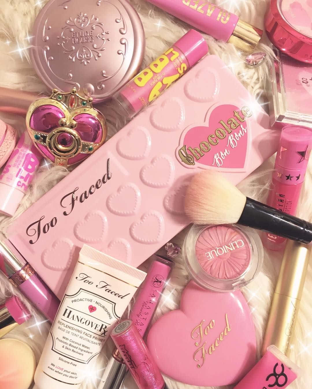 Cosmetic 桌布 壁紙 — 一堆閃閃發光的粉紅色Too Faced化妝品，擺放在蓬鬆的白色毛皮上，帶有閃粉。