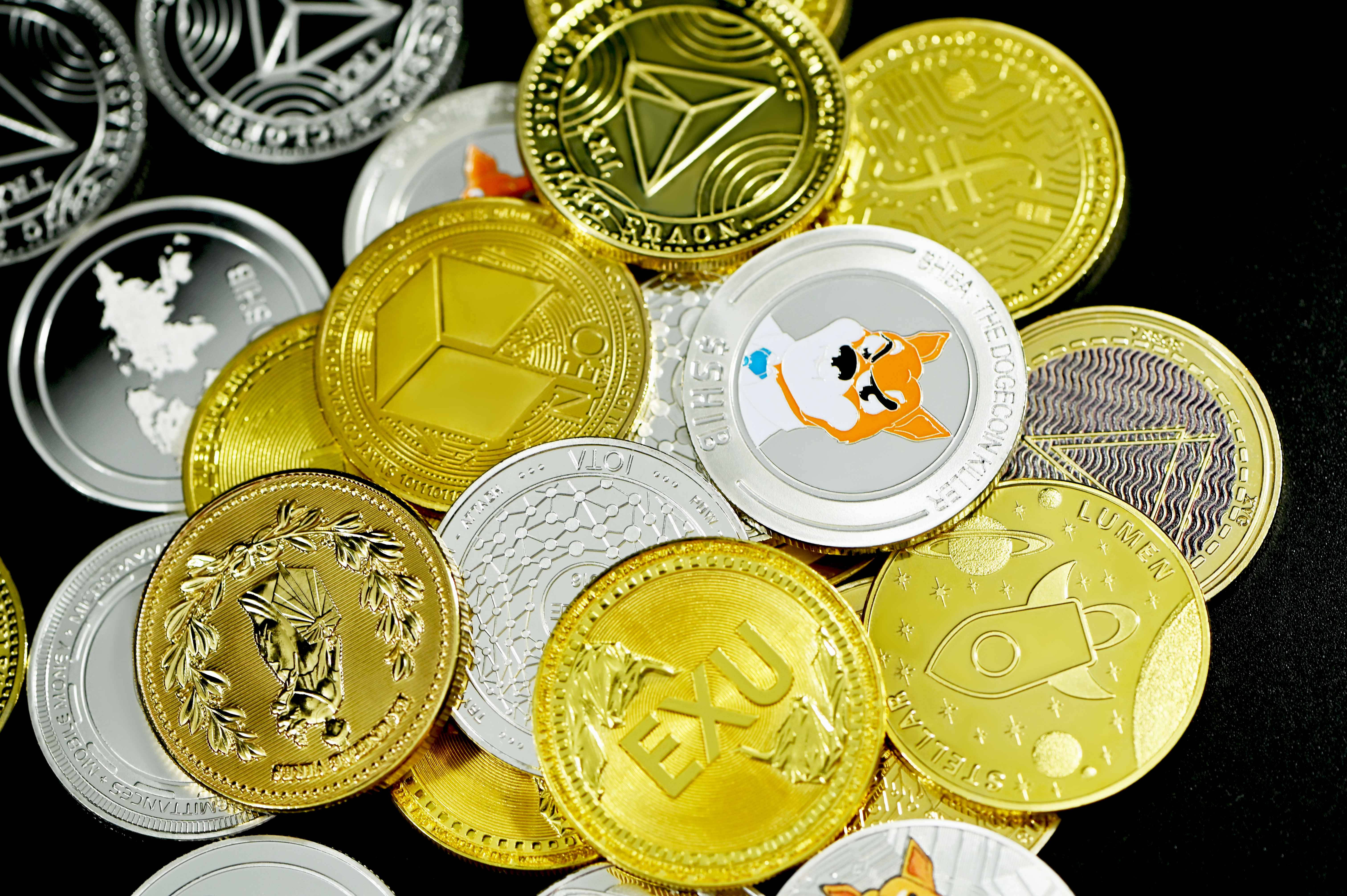 Cryptocurrency 桌布 壁紙 — 一堆閃閃發光的金銀加密貨幣硬幣，帶有獨特標誌，散落在深色表面上。