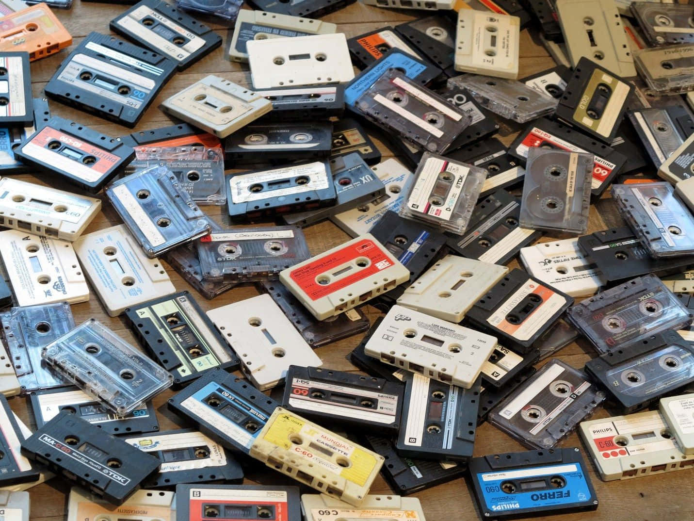 Mixtape 桌布 壁紙 — 一堆雜亂的復古錄音帶，顏色和品牌各異，散落在木質表面上。