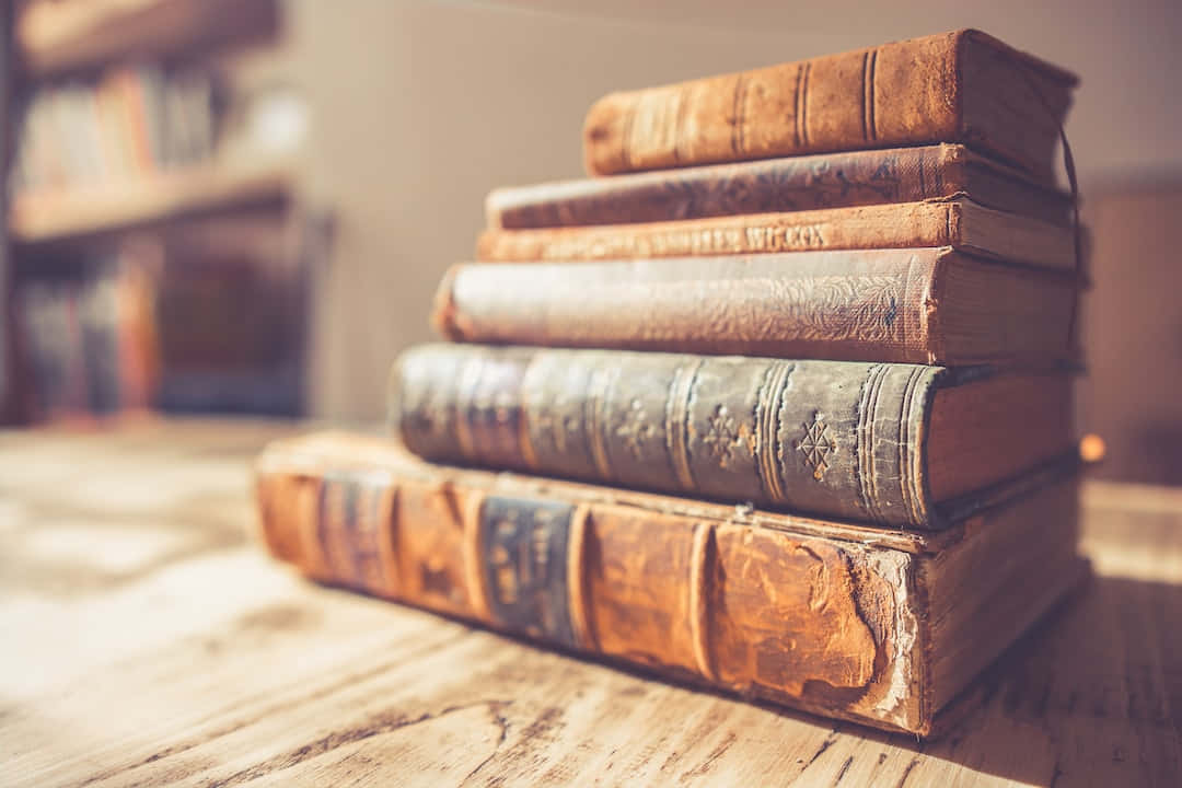 書本 桌布 壁紙 — 一堆風化的復古書籍放在一張沐浴在溫暖金色光線中的木桌上。