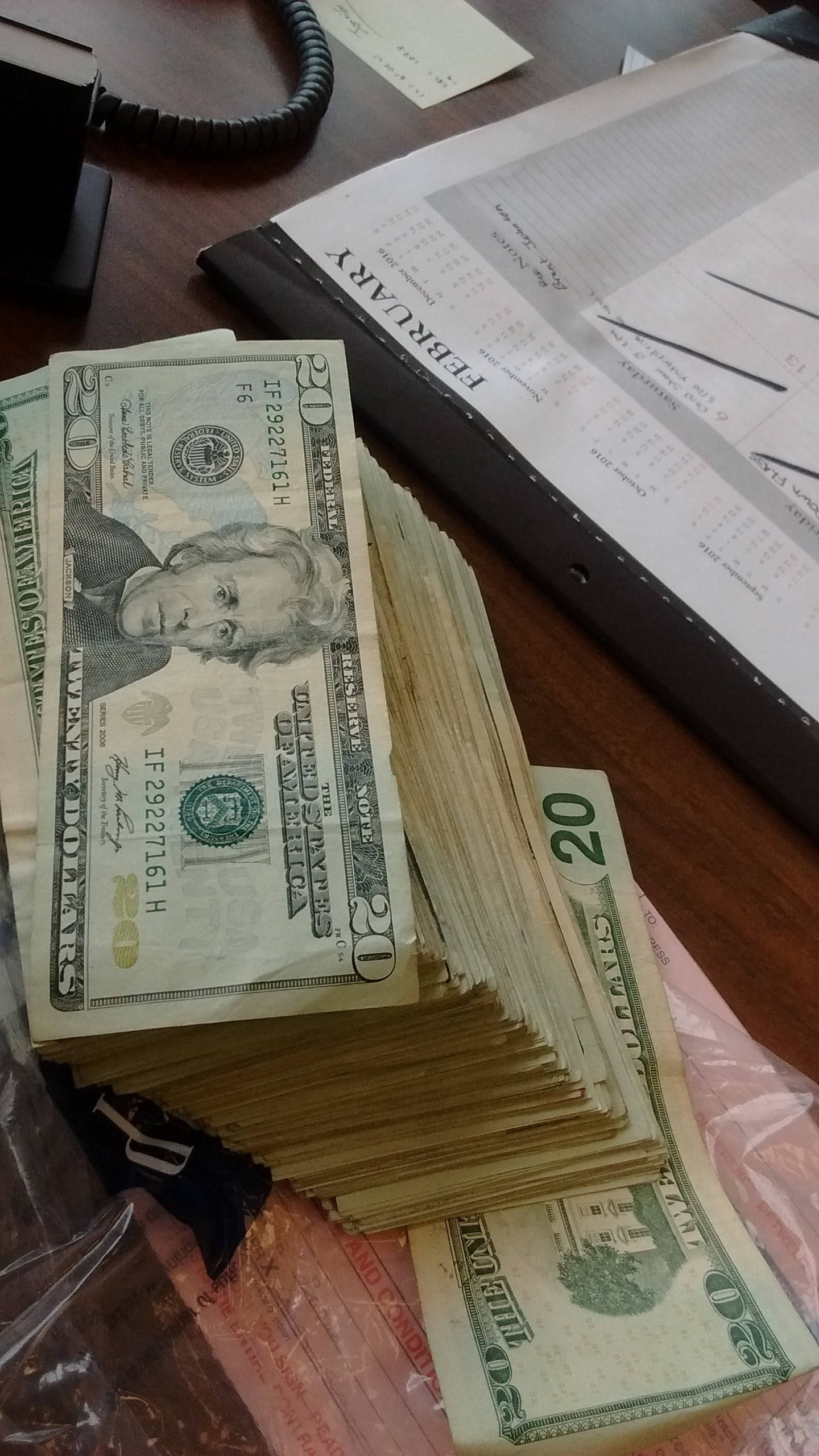 money iPhone 桌布 壁紙 — 一堆高聳的美國二十美元紙幣放在木桌上，旁邊有二月日曆和纏繞的電話線。