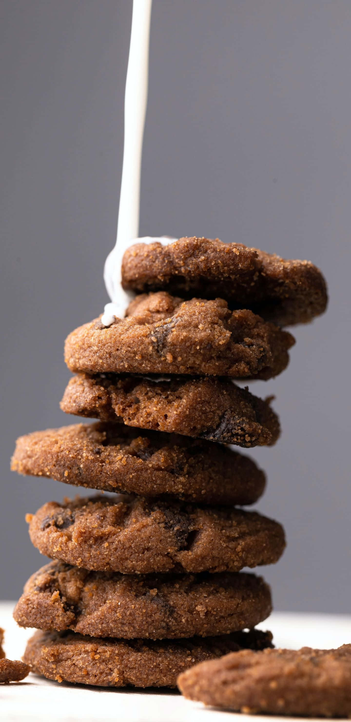 Cookies 桌布 壁紙 — 一堆高高的巧克力餅乾，旁邊有奶油狀的白色牛奶流下，背景為灰色。