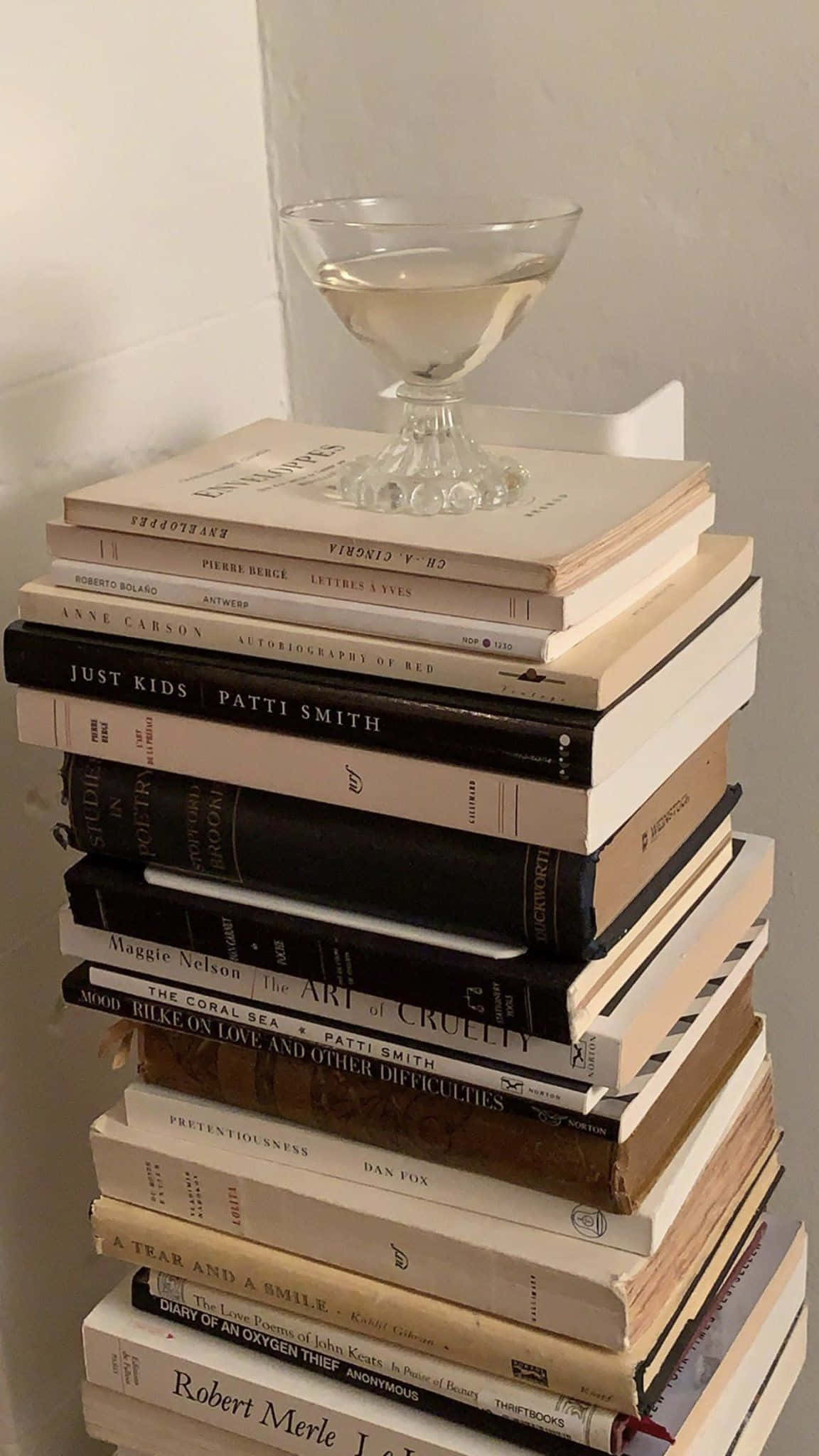 Dark Academia Aesthetic 桌布 壁紙 — 一堆高高的復古書籍，上面平衡地放著一杯香檳杯，背景是素牆。